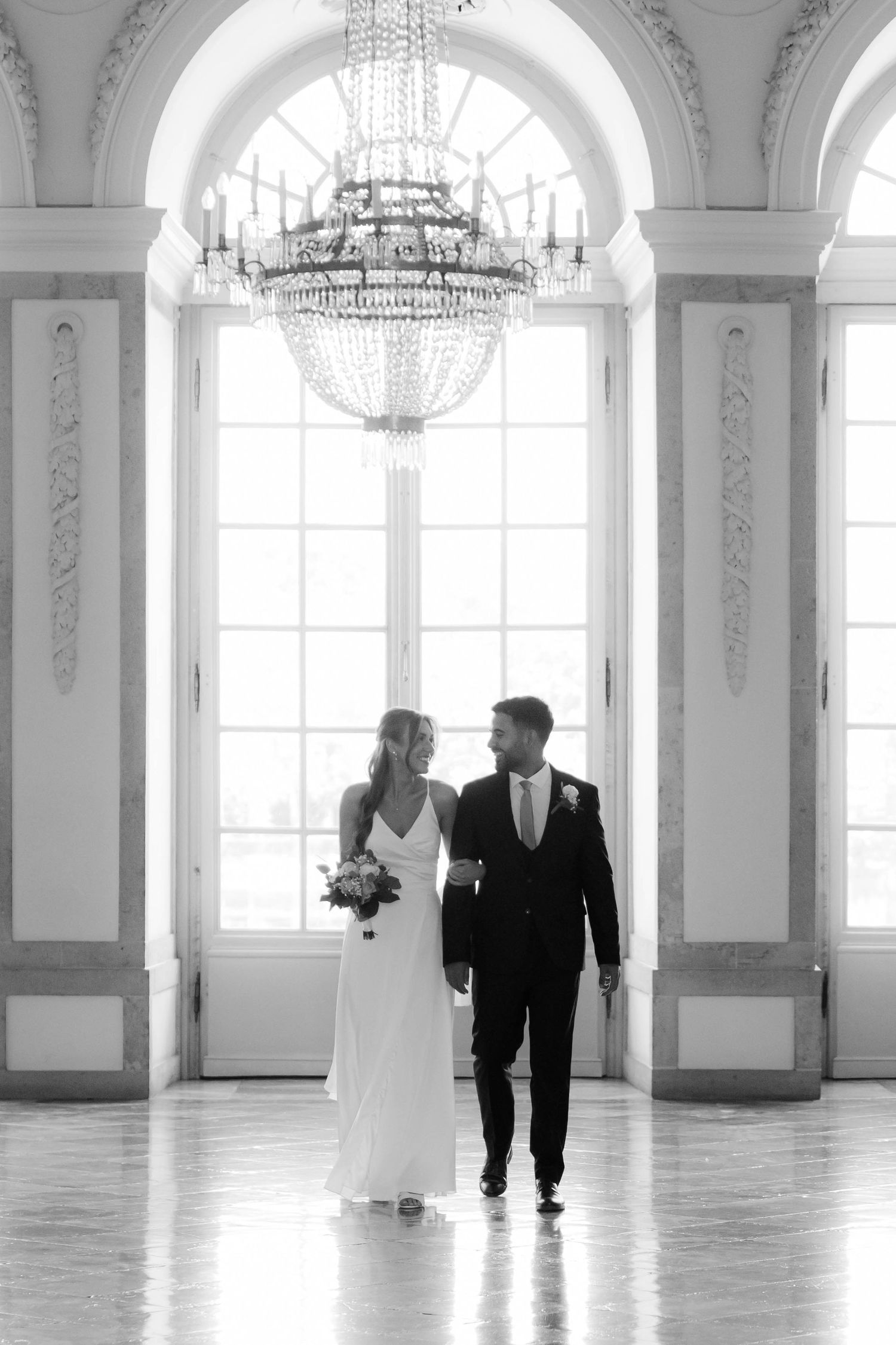 Elegant ballroom interior with crystal chandeliers and arched windows casting natural light.
