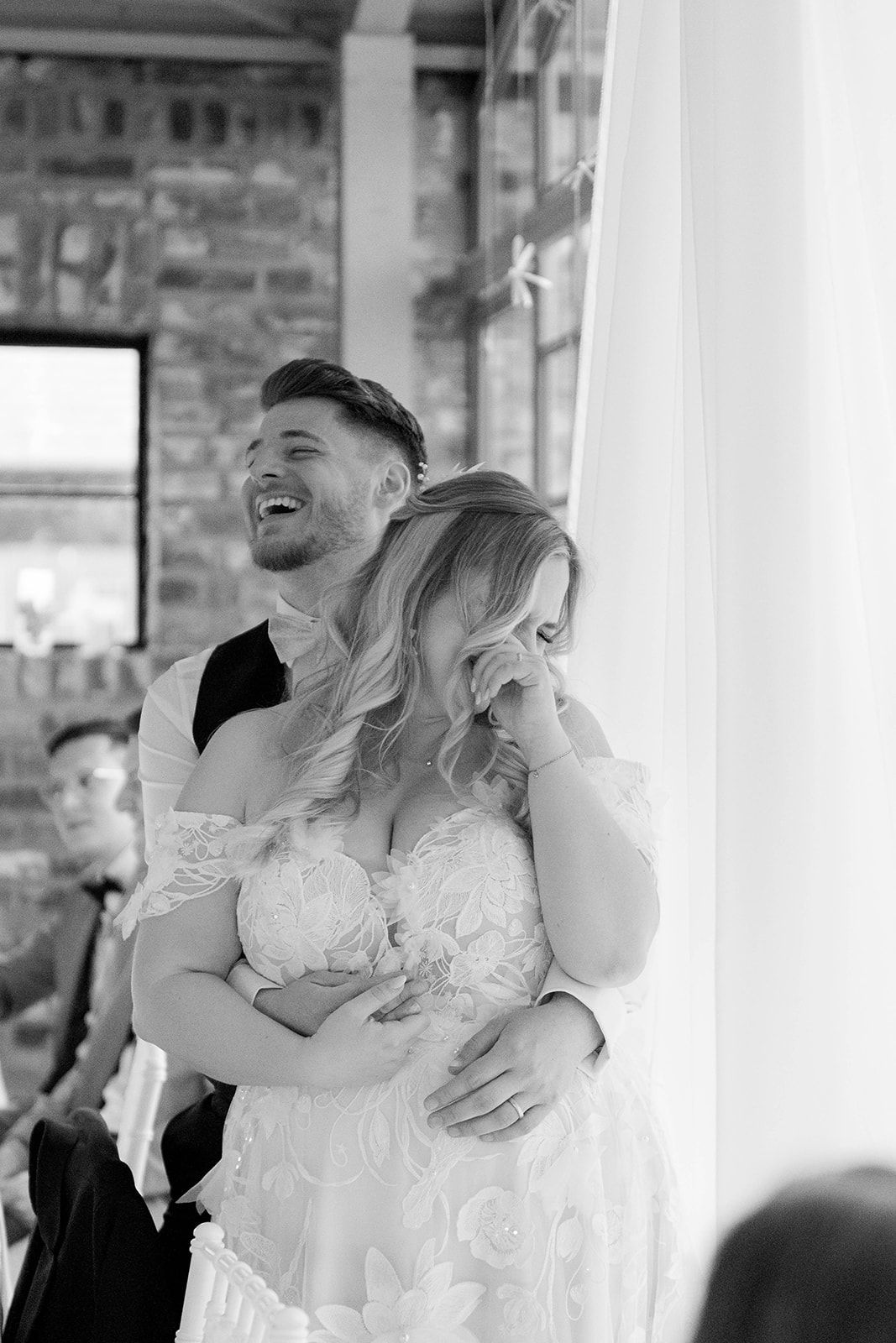 A candid black and white moment of laughter during a wedding reception.