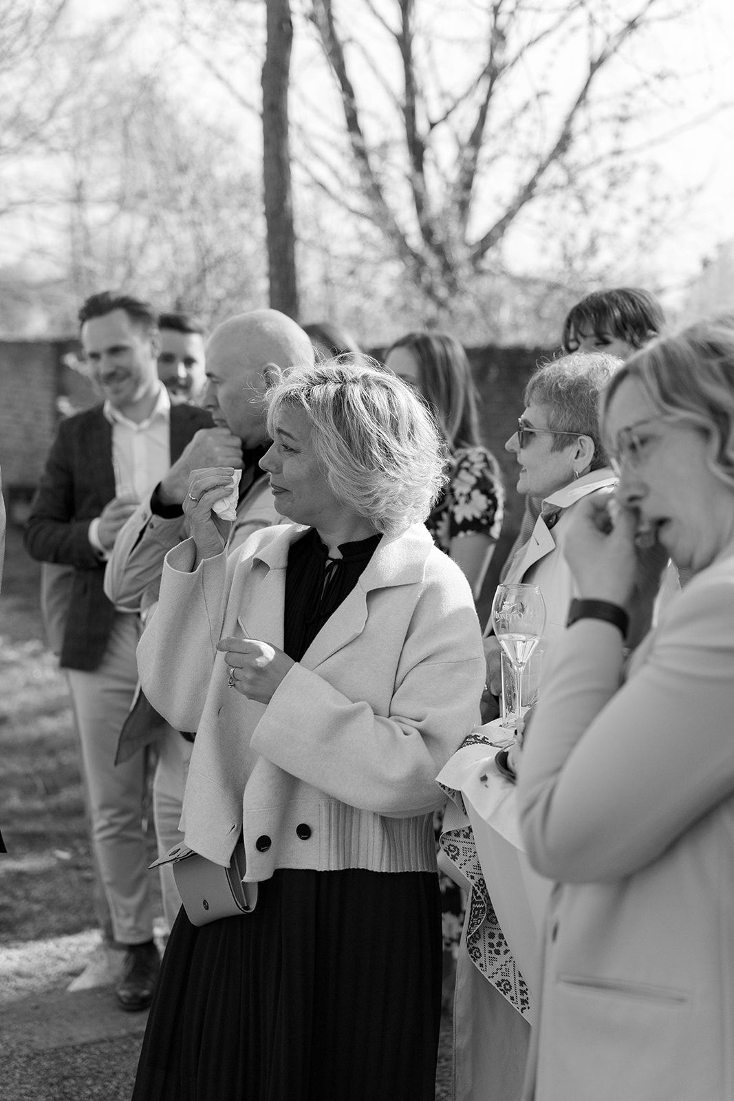 Wedding guests react emotionally during an outdoor ceremony in black and white photography.
