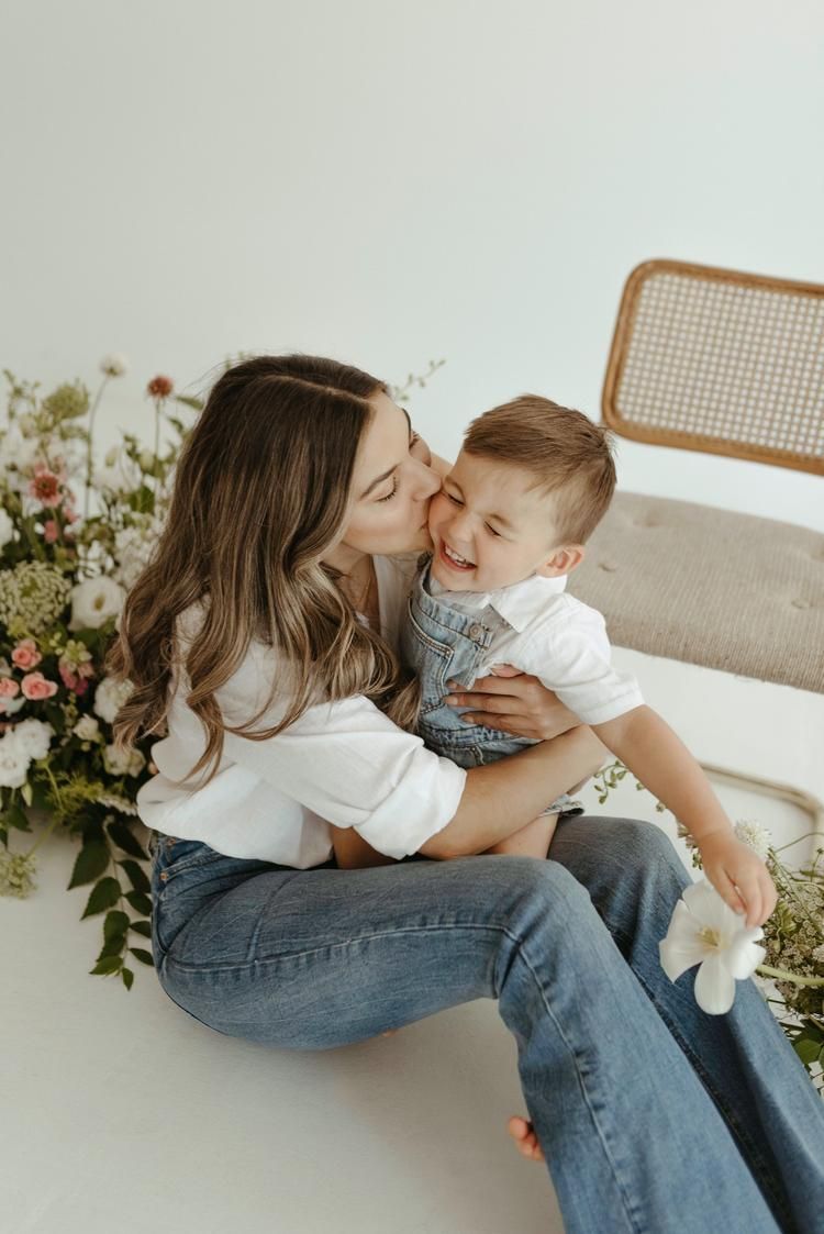 A tender moment shared between parent and child while relaxing on a light colored couch with greenery in the background.
