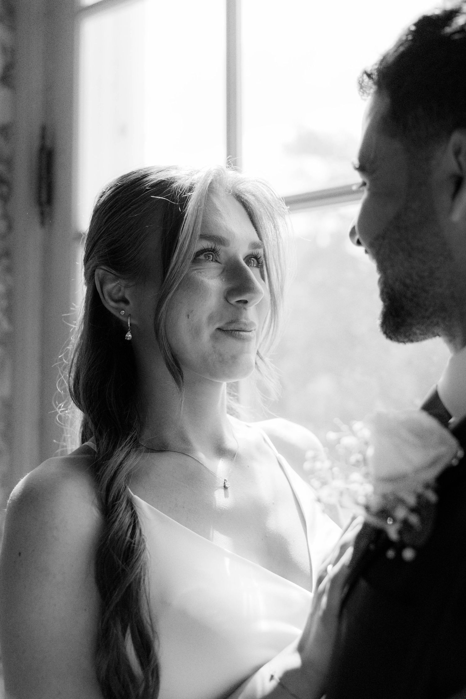 Soft backlit window portrait capturing an intimate moment in black and white.