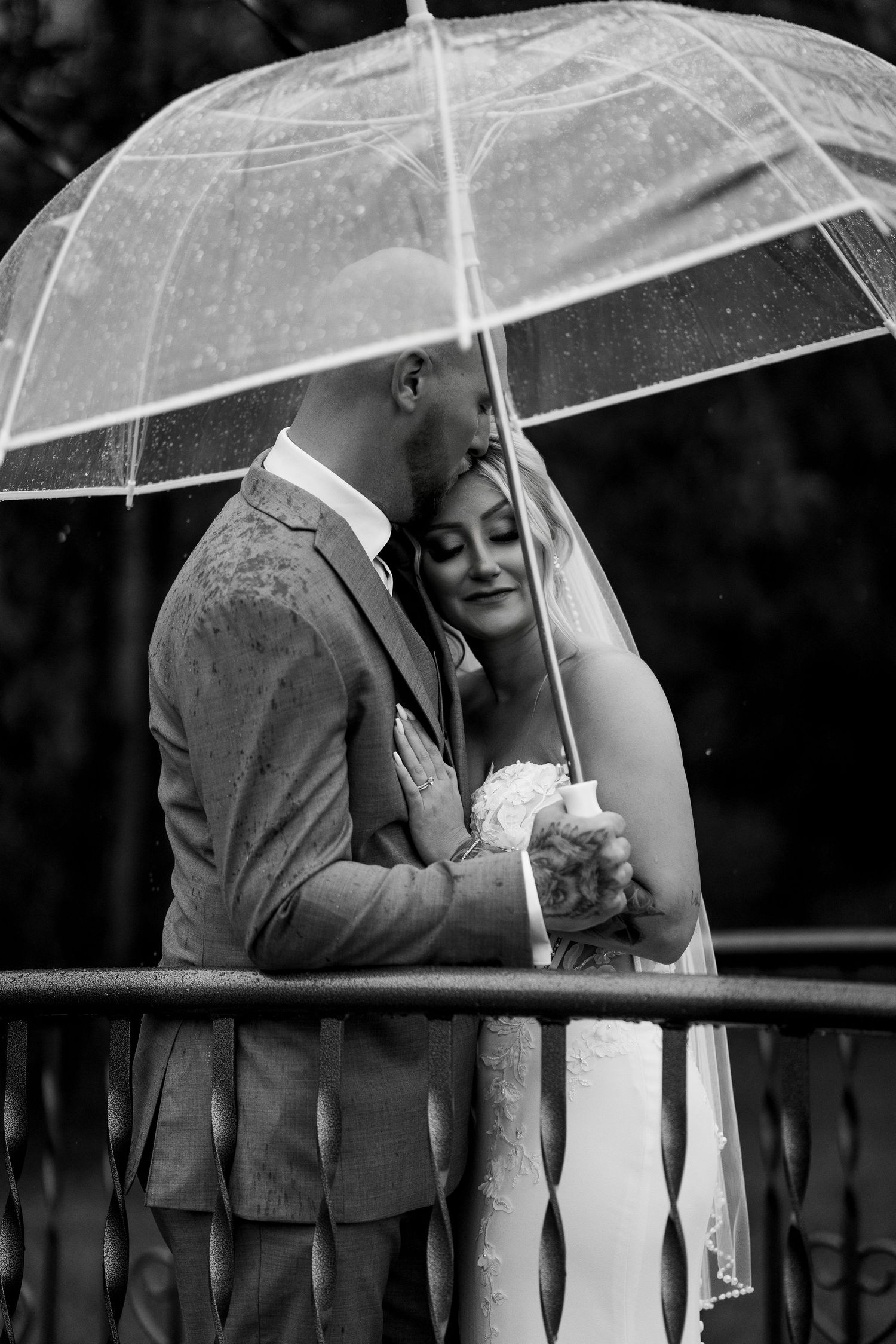 Bride and groom embrace under an umbrella during their newlywed portraits in a rainstorm during their wedding day in Grande Prairie Alberta