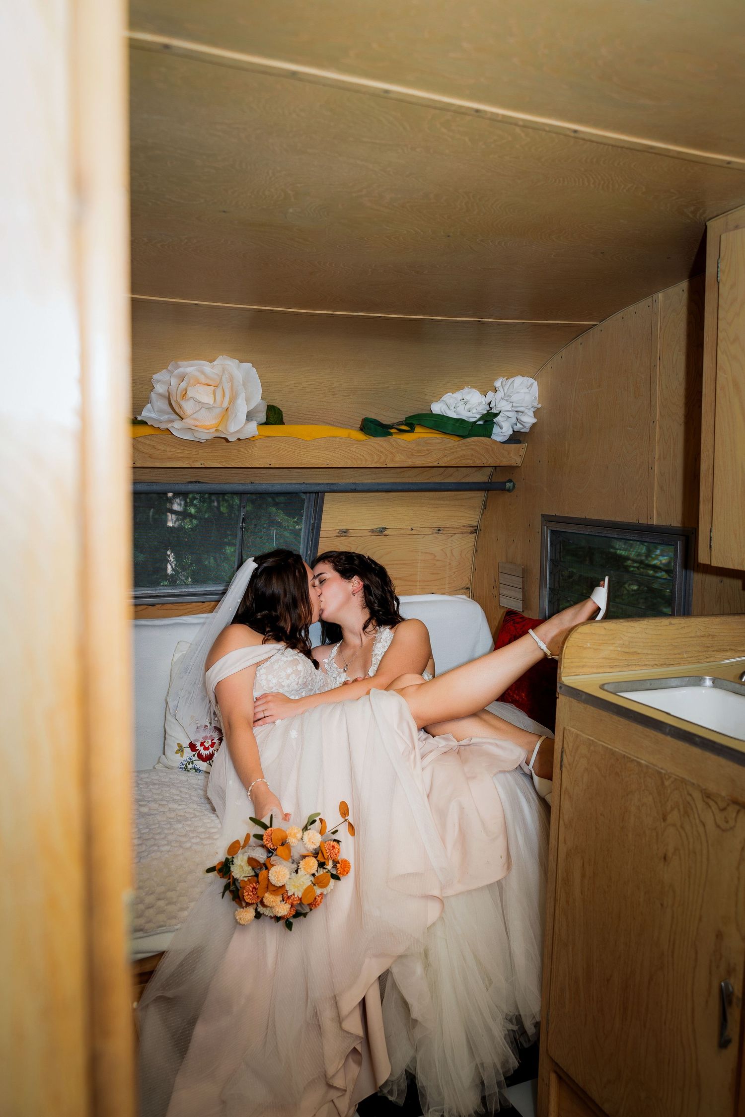 Playful luxury wedding photo of two brides kissing in camper trailer after ceremony, capturing joyful and intimate LGBTQ+ wedding moments.