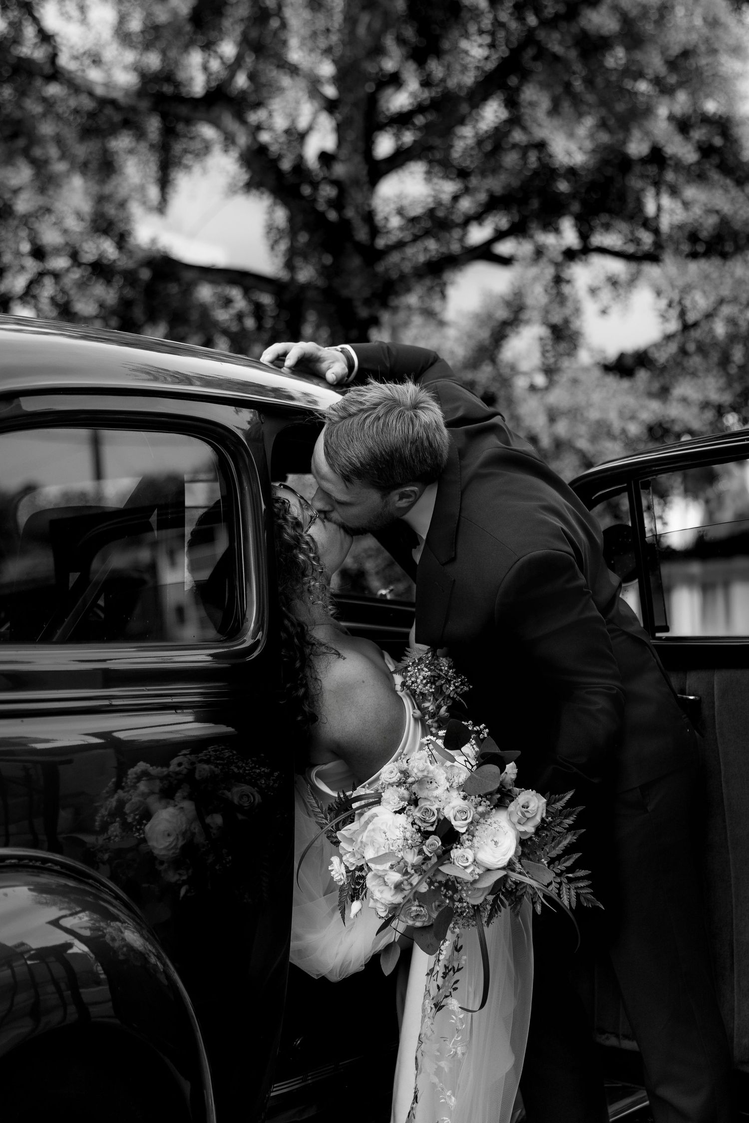 Stylish wedding photo of bride and groom kissing in getaway car outside Kamloops Courthouse, capturing romantic, memorable wedding moments.