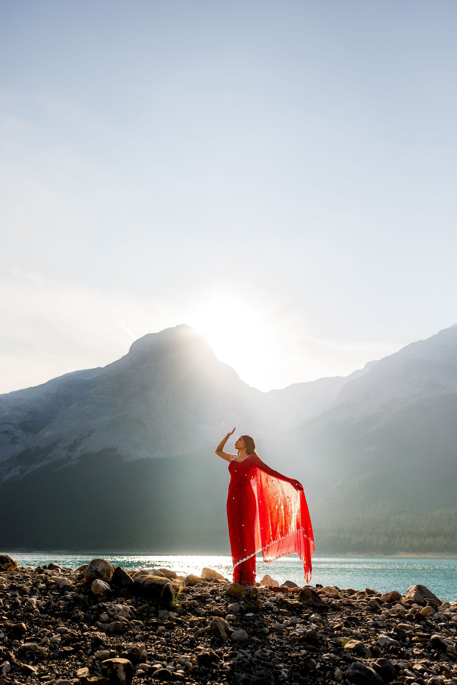 Luxury portrait of a woman in a red saree standing in the mountains of Kananaskis for her engagement photography session.