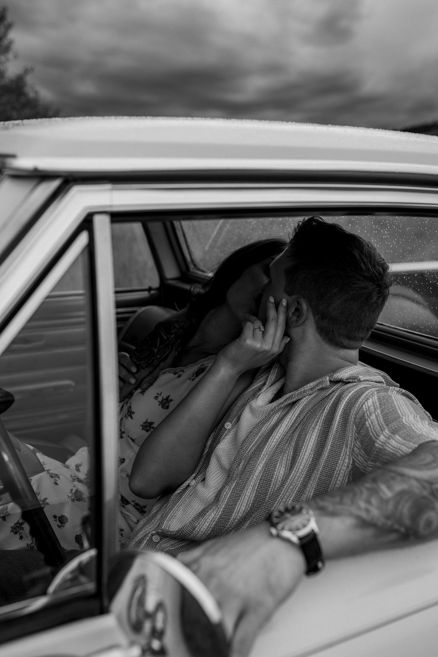 Luxury engagement photo of couple in front of vintage car, focus on bride’s ring, capturing romantic and stylish engagement photography.