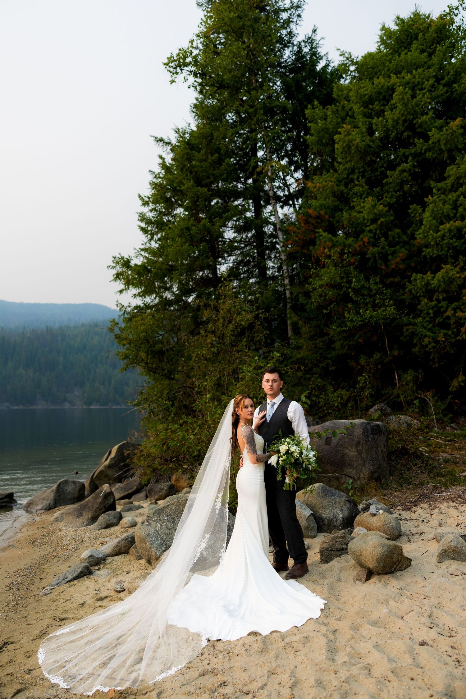 Stunning wedding portrait of newlyweds on a British Columbia beach with mountain backdrop, capturing romantic and scenic destination wedding