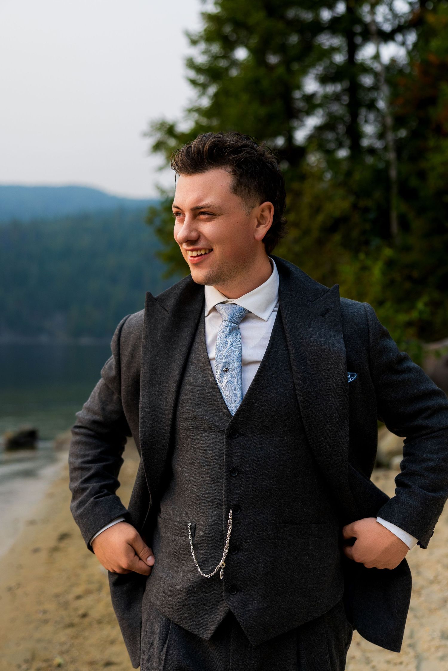 Groom poses for portraits in his elegant suit and groom detail accessories at destination wedding in British Columbia.