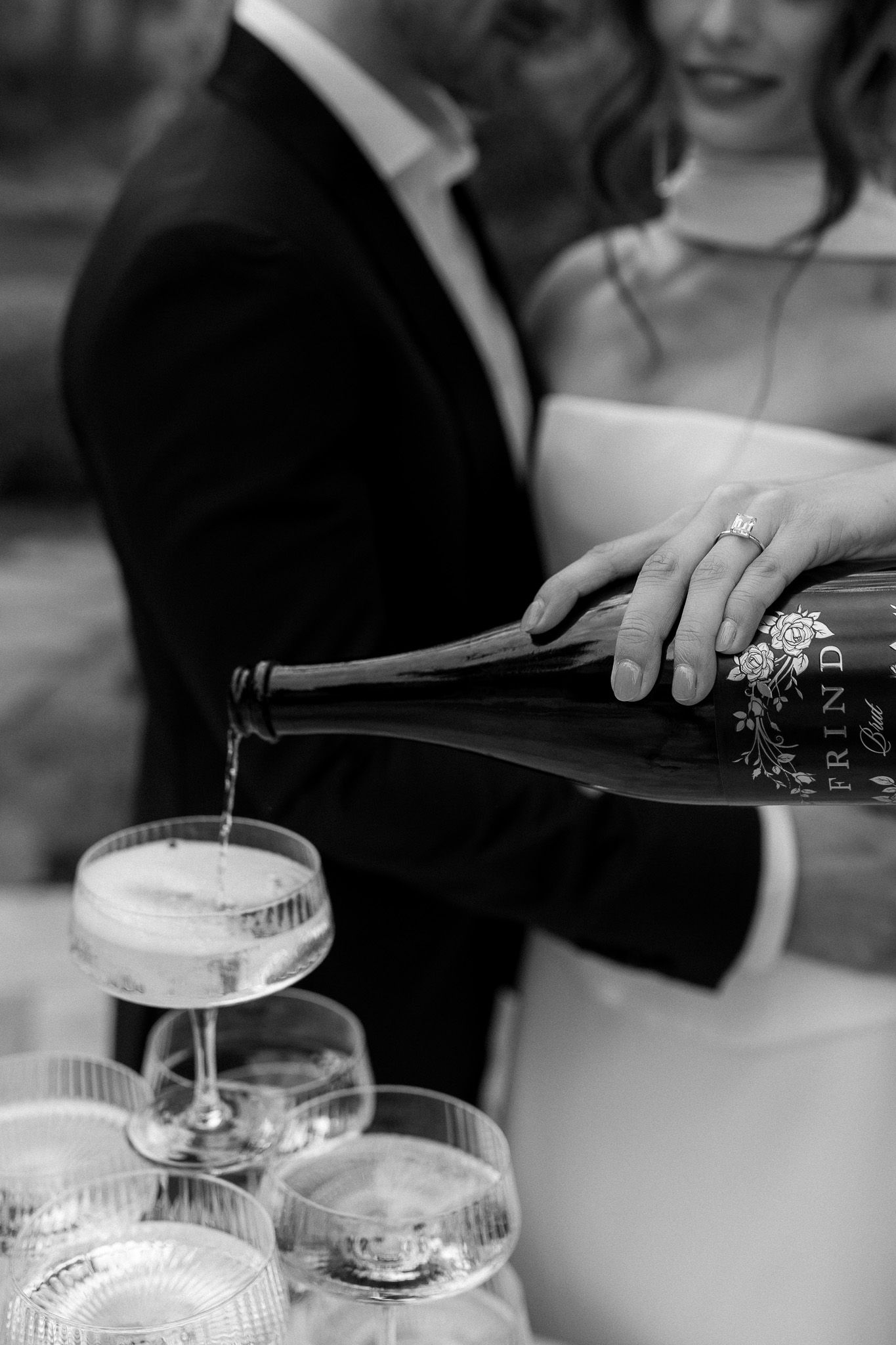 Bride pours bottle for champagne tower photos that are editorial and luxury, flash photography by professional wedding photographer.