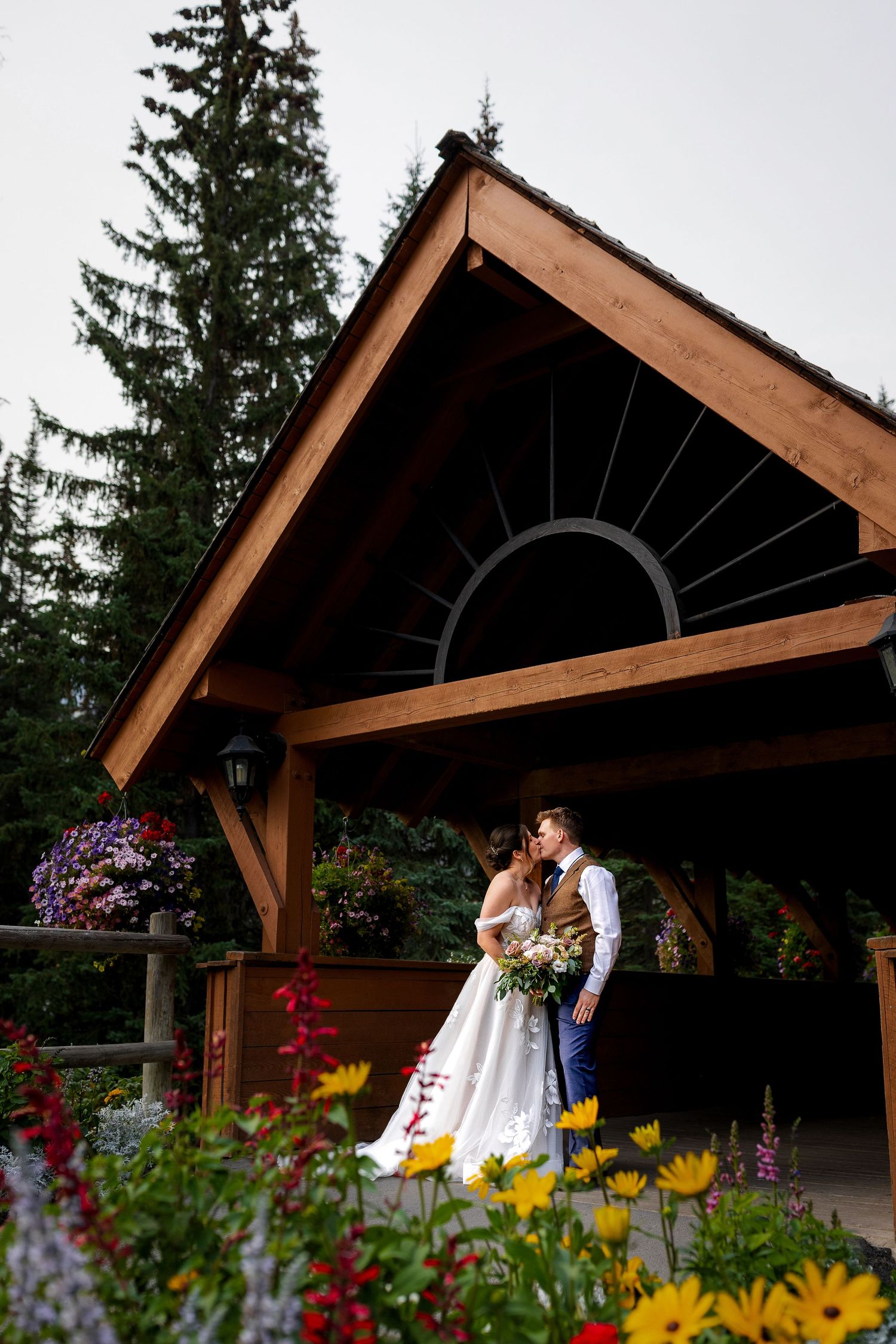 Luxury wedding photo of bride and groom kissing under bridge at Sun Peaks Resort, capturing romantic and stylish destination wedding photos.