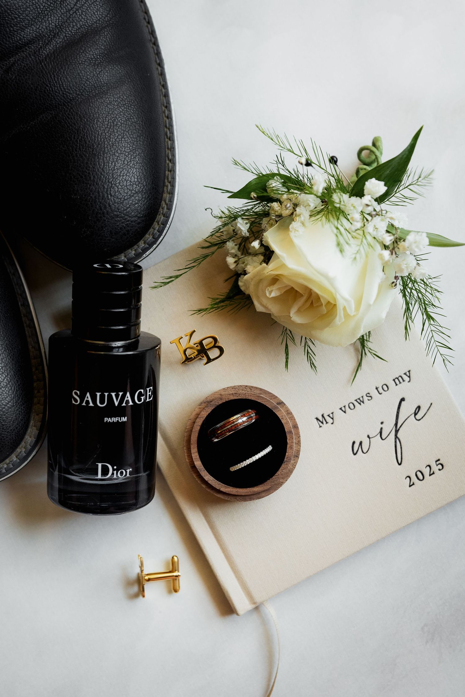 Wedding detail flat lay of groom’s cologne, rings, and vow book, capturing stylish and elegant wedding preparation photography.