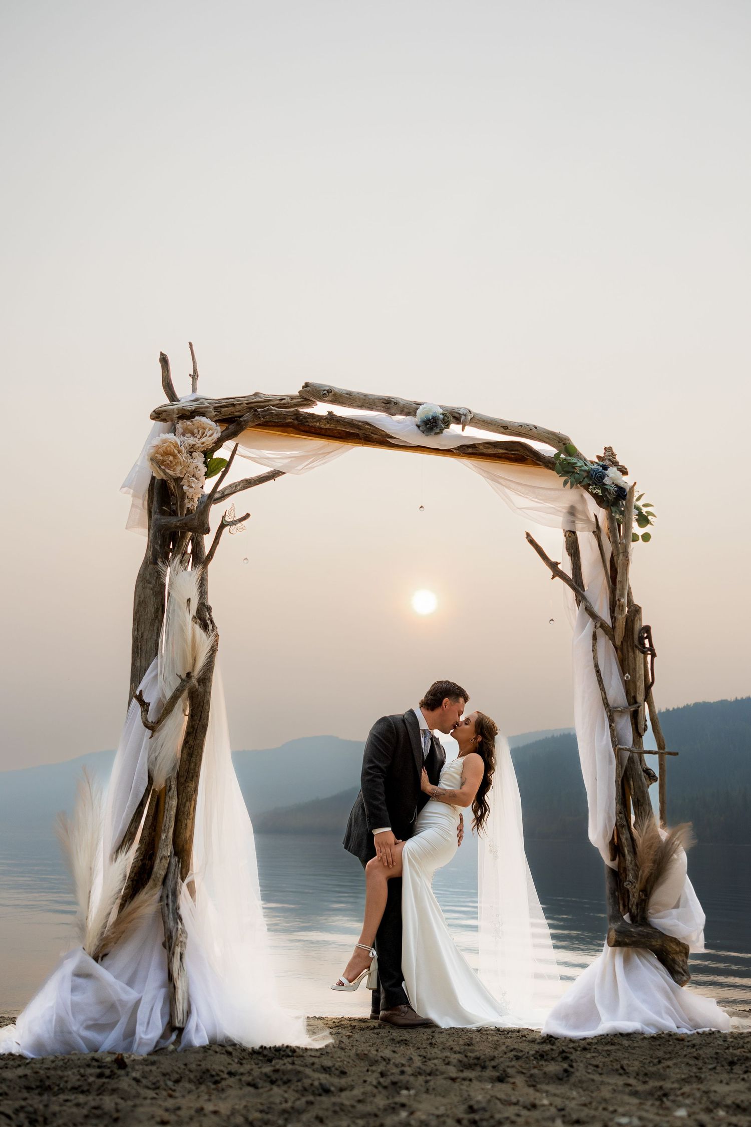 Luxury wedding photo of bride and groom kissing under ceremony arch, capturing romantic, and stylish destination wedding photography.