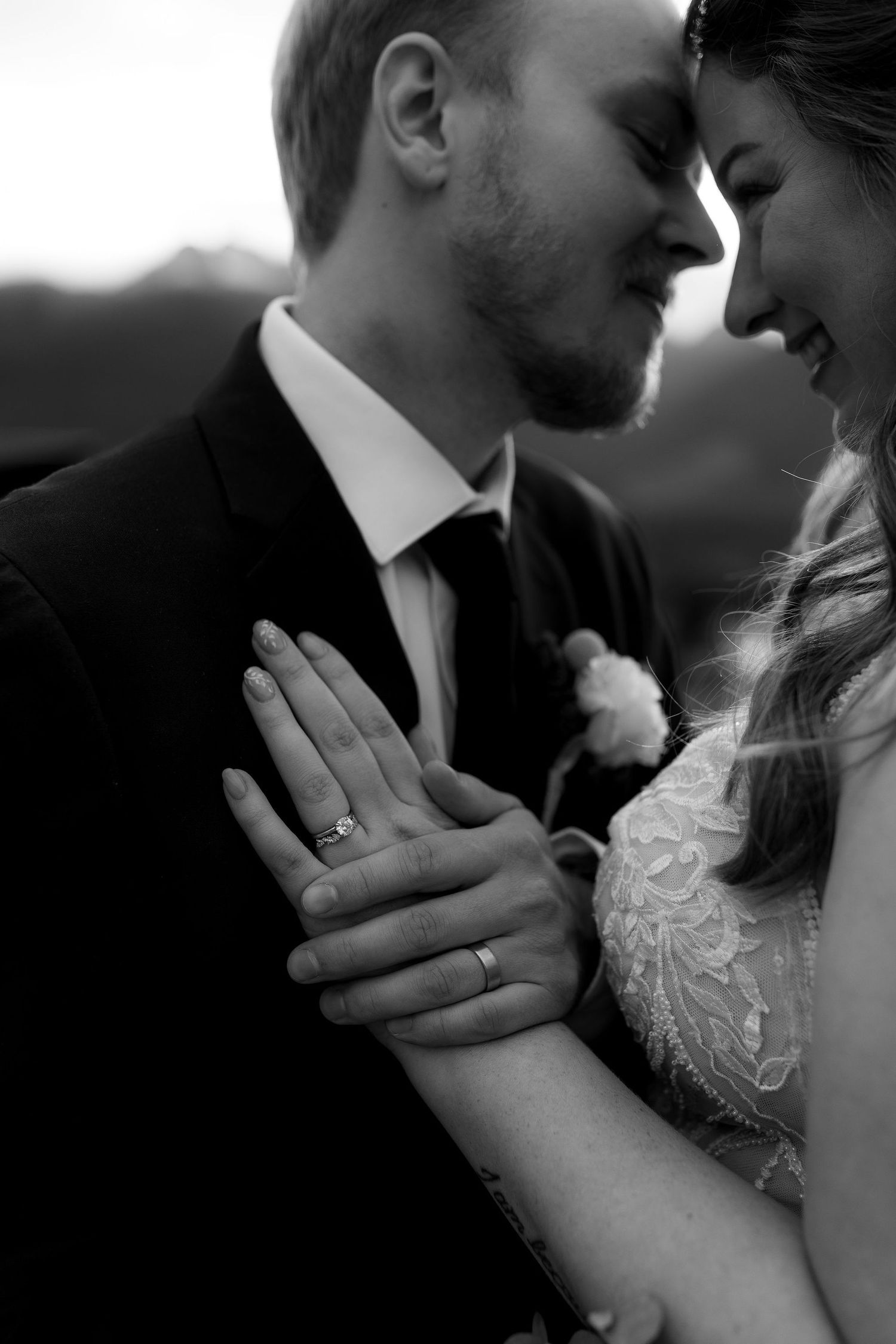 Black and white wedding photo of bride and groom, hands resting on groom’s chest with wedding rings in focus, capturing newlywed bliss.