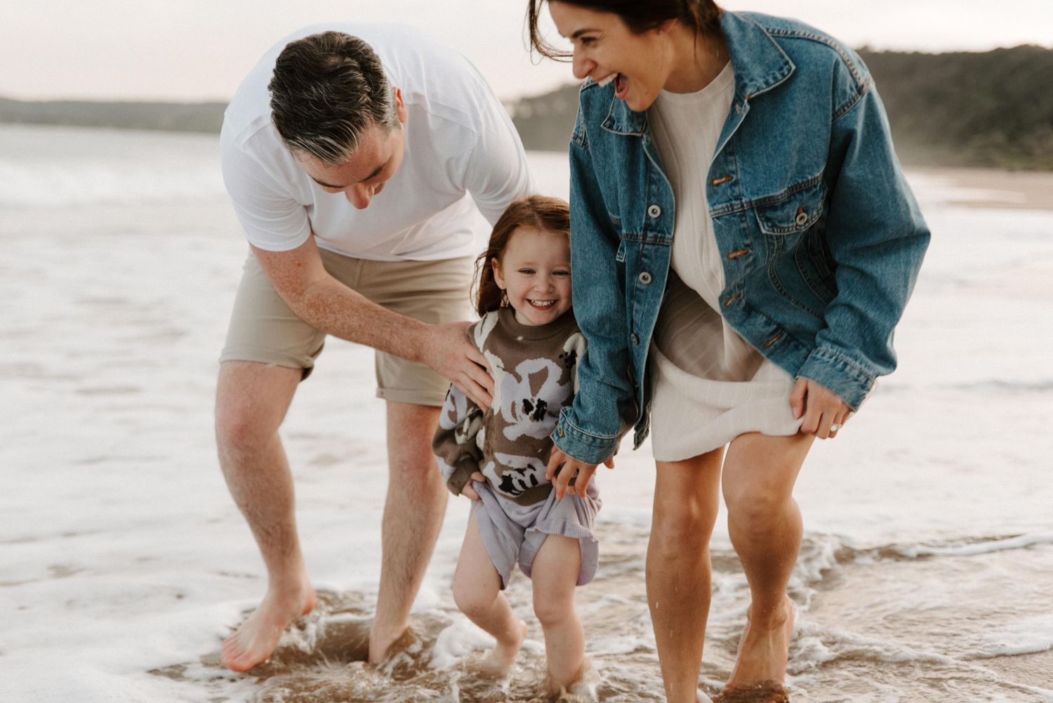family in coordinating outfits during their beach session splashing in the waves