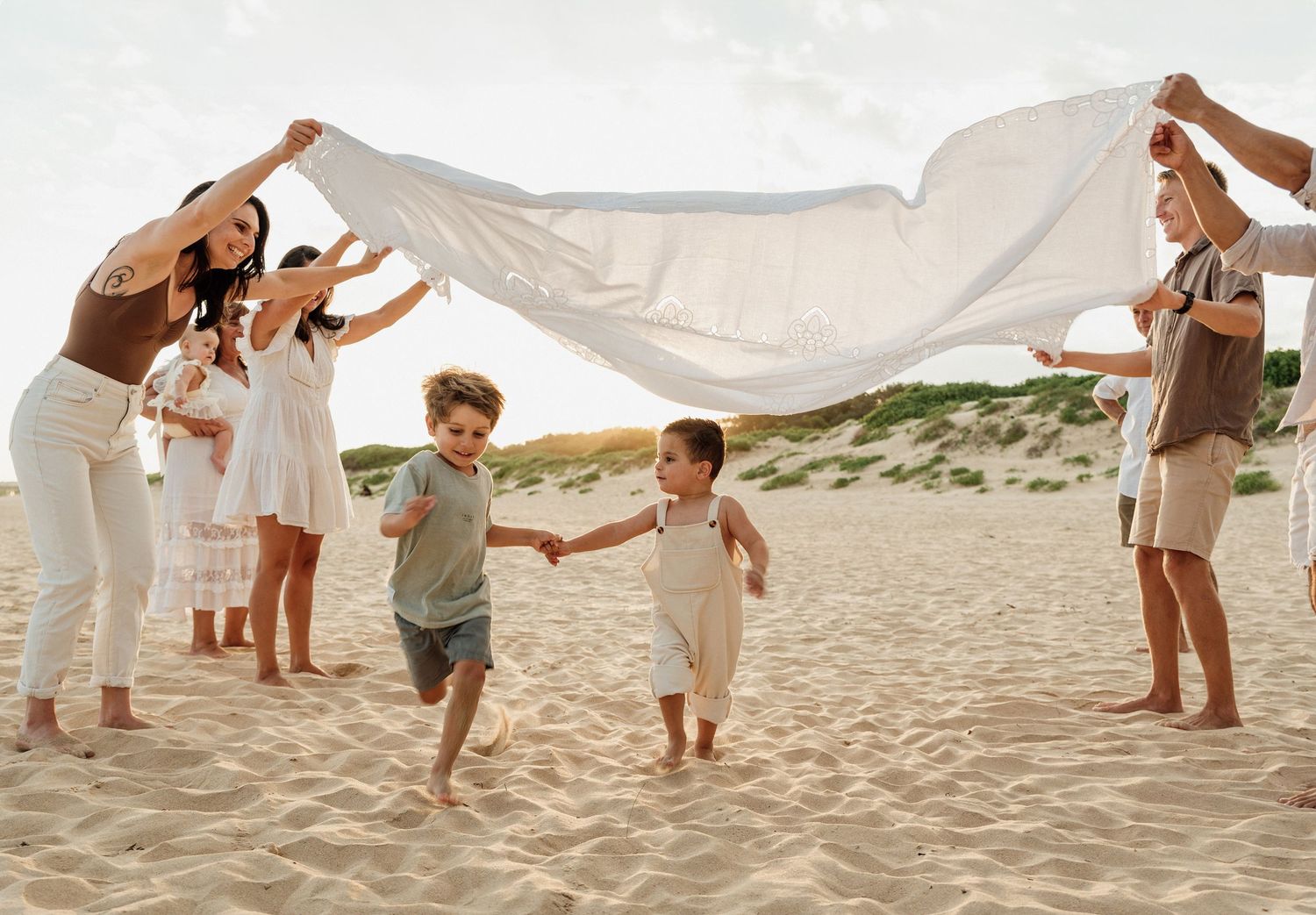 Family session at the beach with two boys running under a blanket in the air