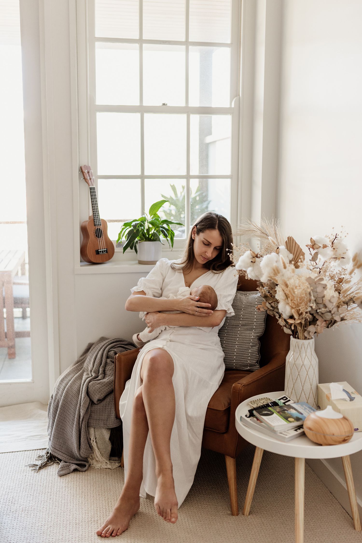 Mother sitting by a window gazing at her newborn sleeping baby