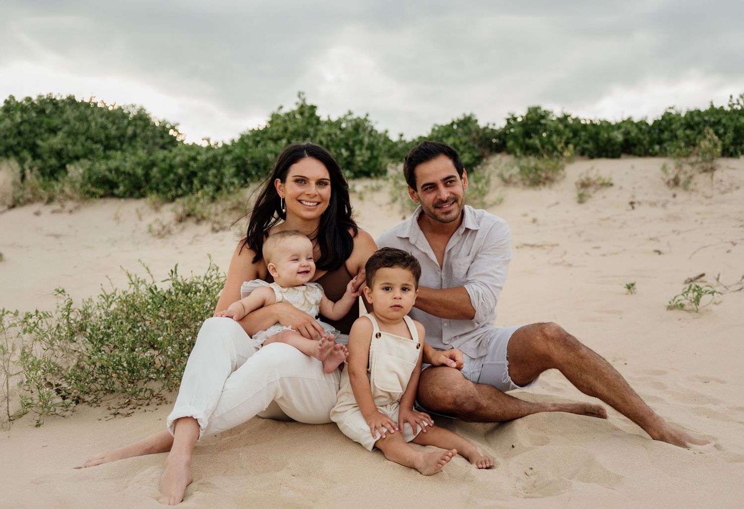 Family in neutral outfits sitting on the beach for photoshoot