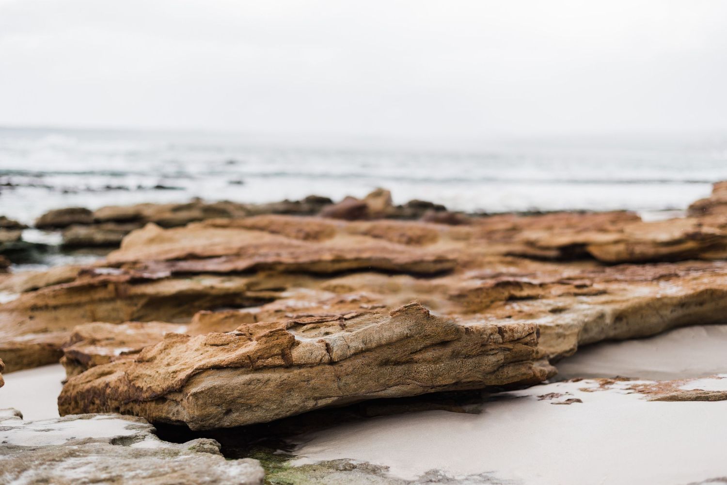 Natural sandstone rock formation on a serene beach with grey overcast sky and ocean view.