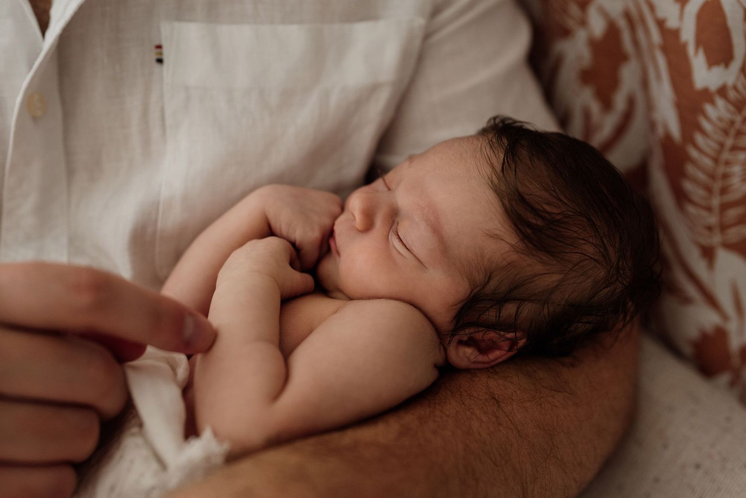 Peaceful newborn baby sleeping curled up on fathers chest in soft natural light.