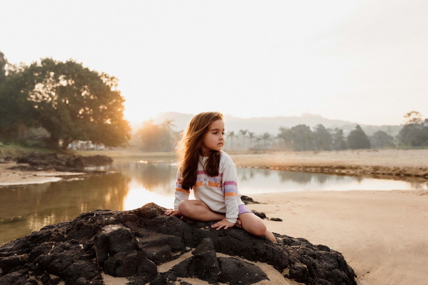 Girl sitting on rocks at beach in Kiama at sunset.