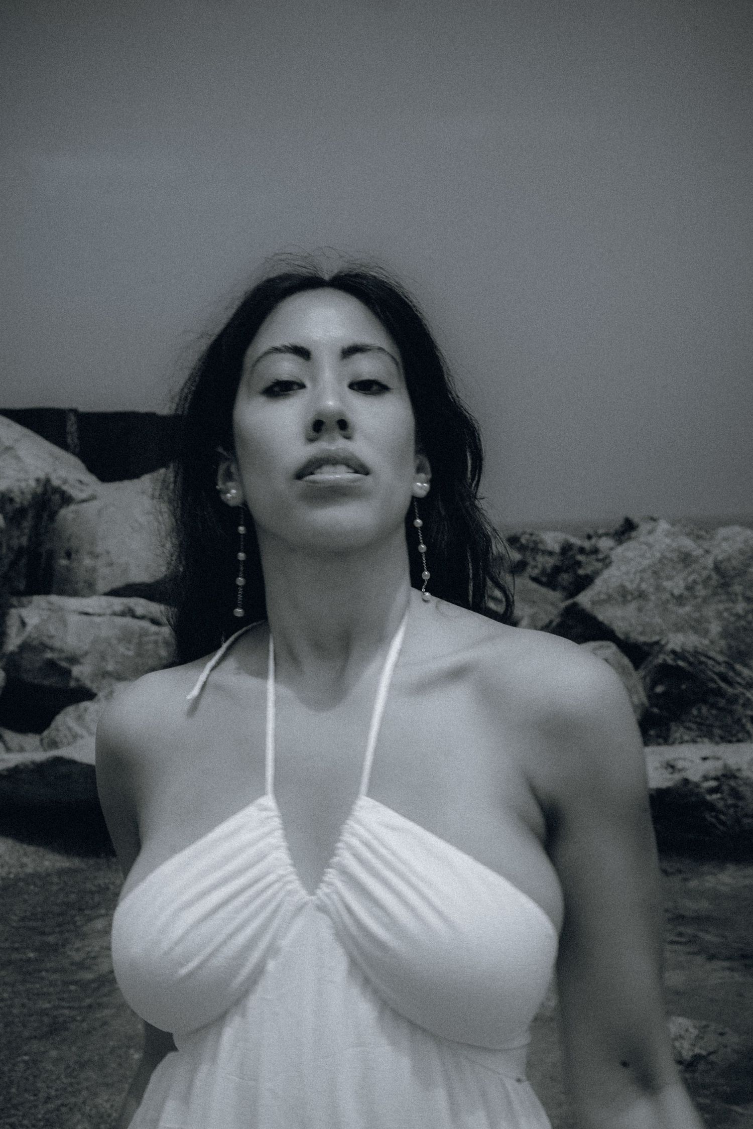 Woman in white halter dress poses near rocks in black and white photo wearing drop earrings.