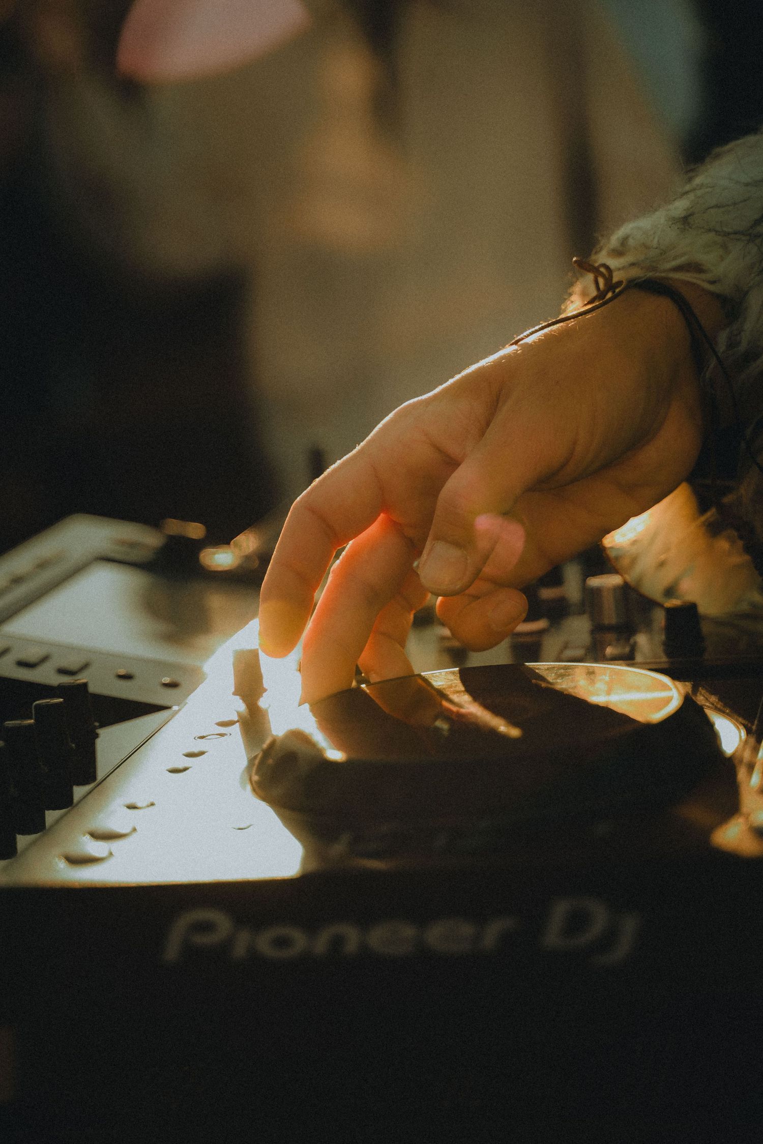 Close-up of hands adjusting controls on a Pioneer DJ mixer deck in dim lighting.
