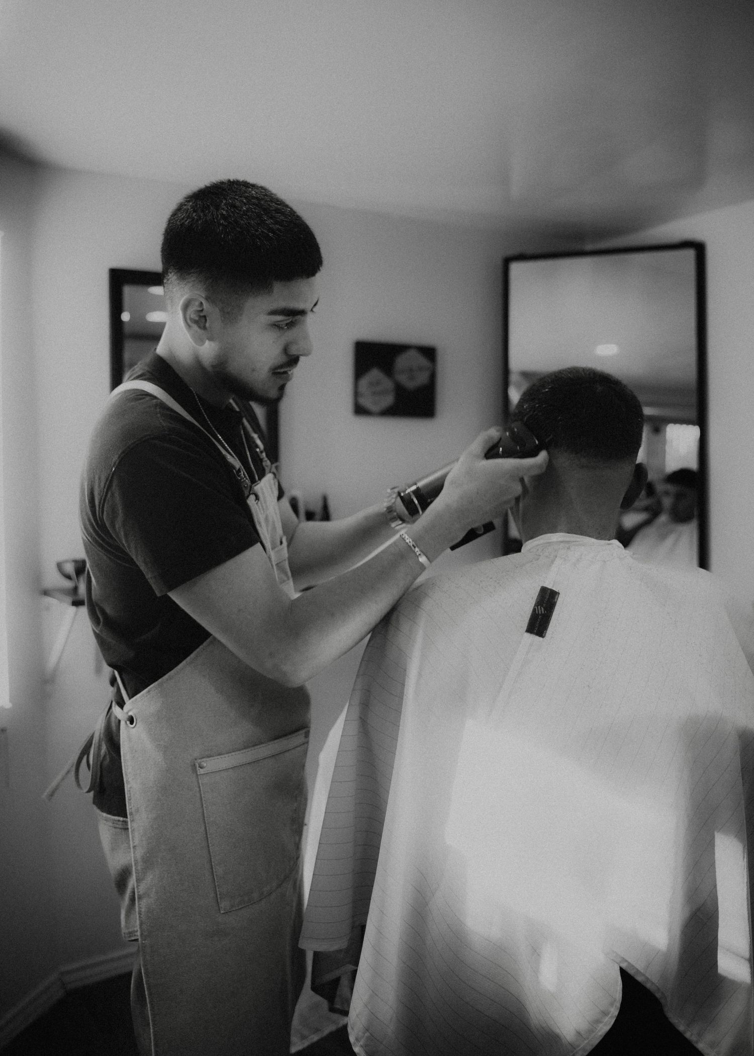 A barber uses scissors and comb to give a precise haircut to a client in a monochromatic barbershop setting.