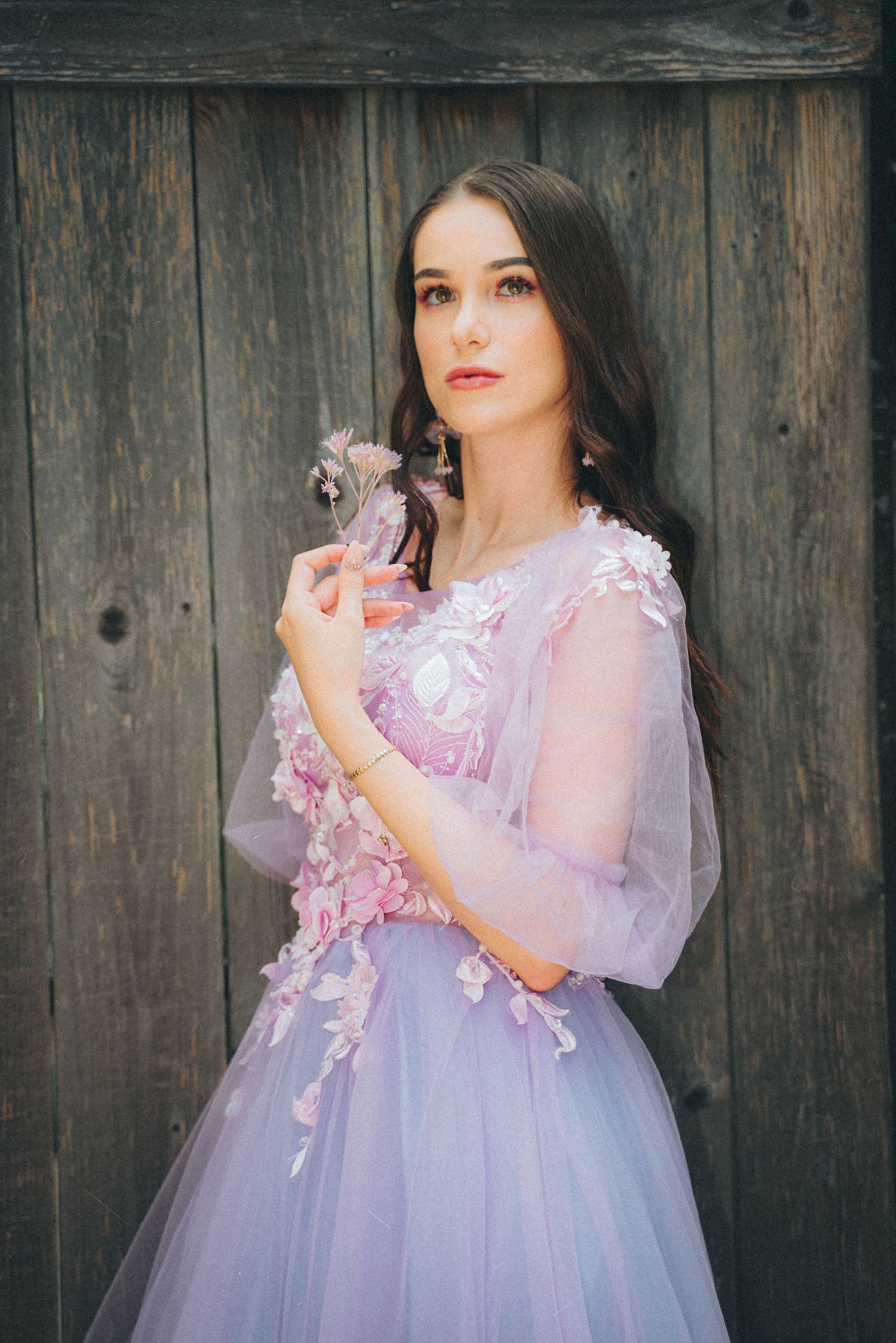 Ethereal portrait in a lavender tulle gown with floral appliques against rustic wooden backdrop.