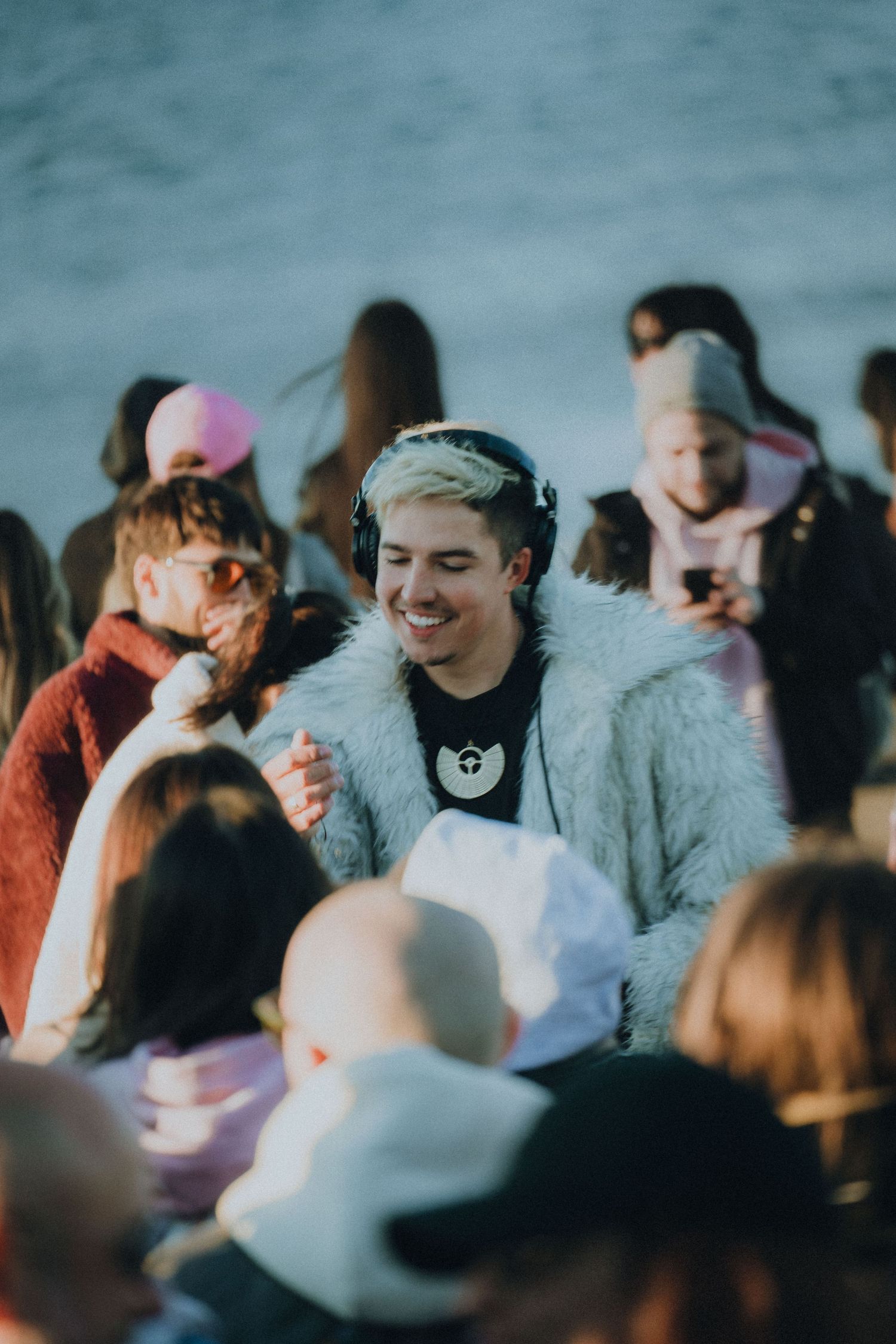 A blurred crowd of concert attendees enjoying themselves with smiles and winter clothing in an outdoor setting.