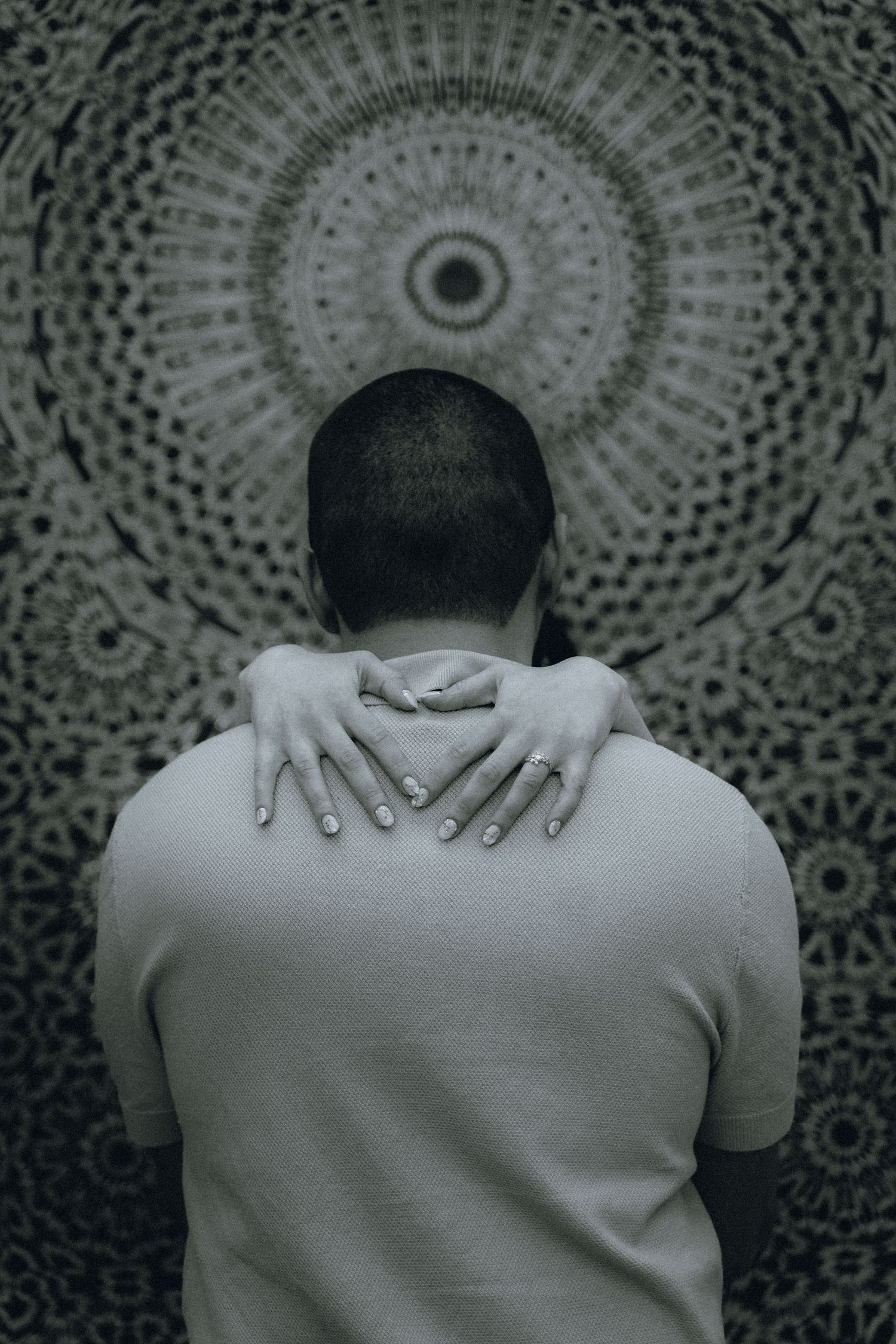 Black and white artistic photo series showing hands placed on shoulders against a patterned circular background.
