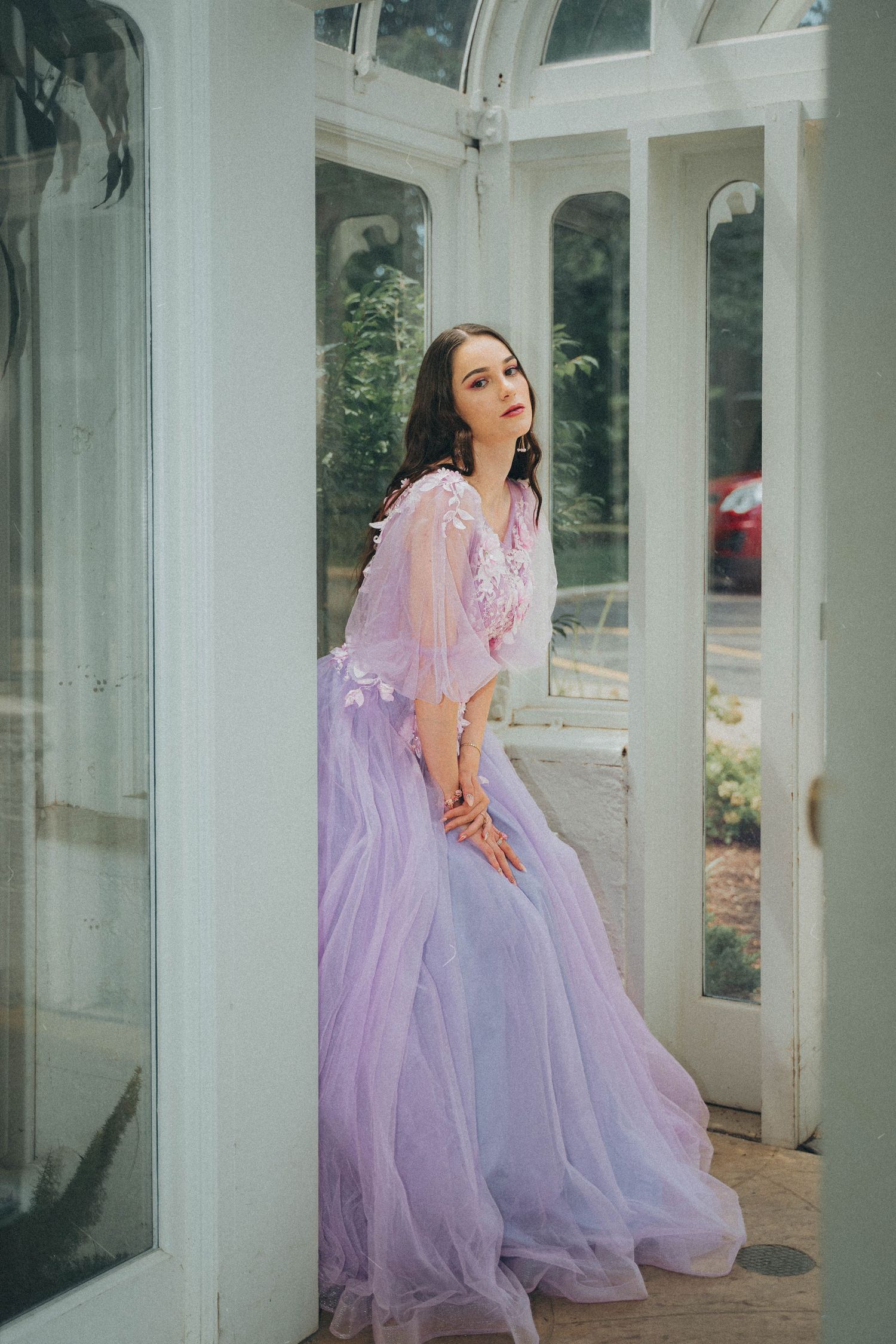 A dreamy sequence of someone in a flowing lavender tulle gown posing gracefully against white columns in a garden setting.