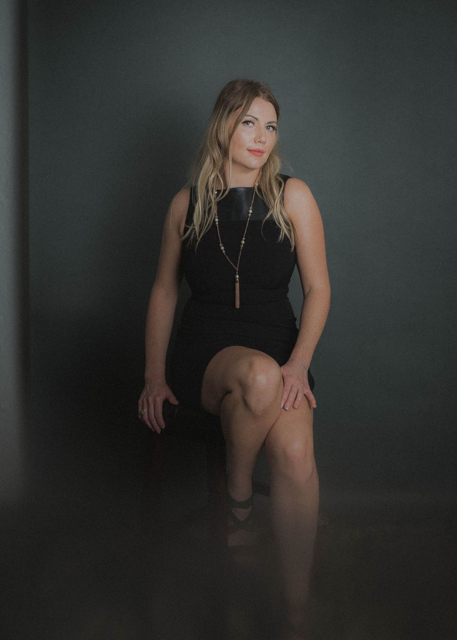 Black and white photo series shows woman in dark dress posing in dramatic moody lighting against textured wall.