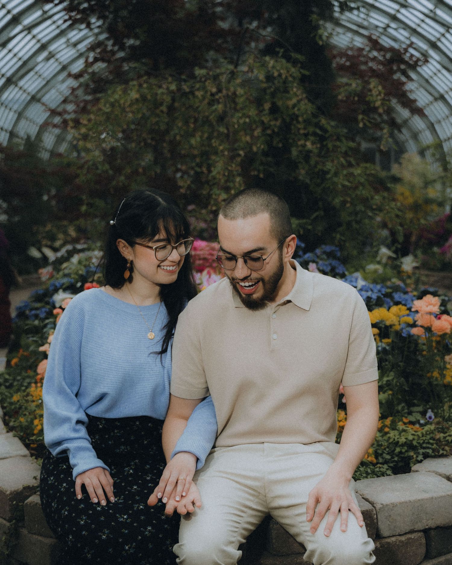 A couple sits together on stone steps in a garden filled with blooming flowers and greenery.