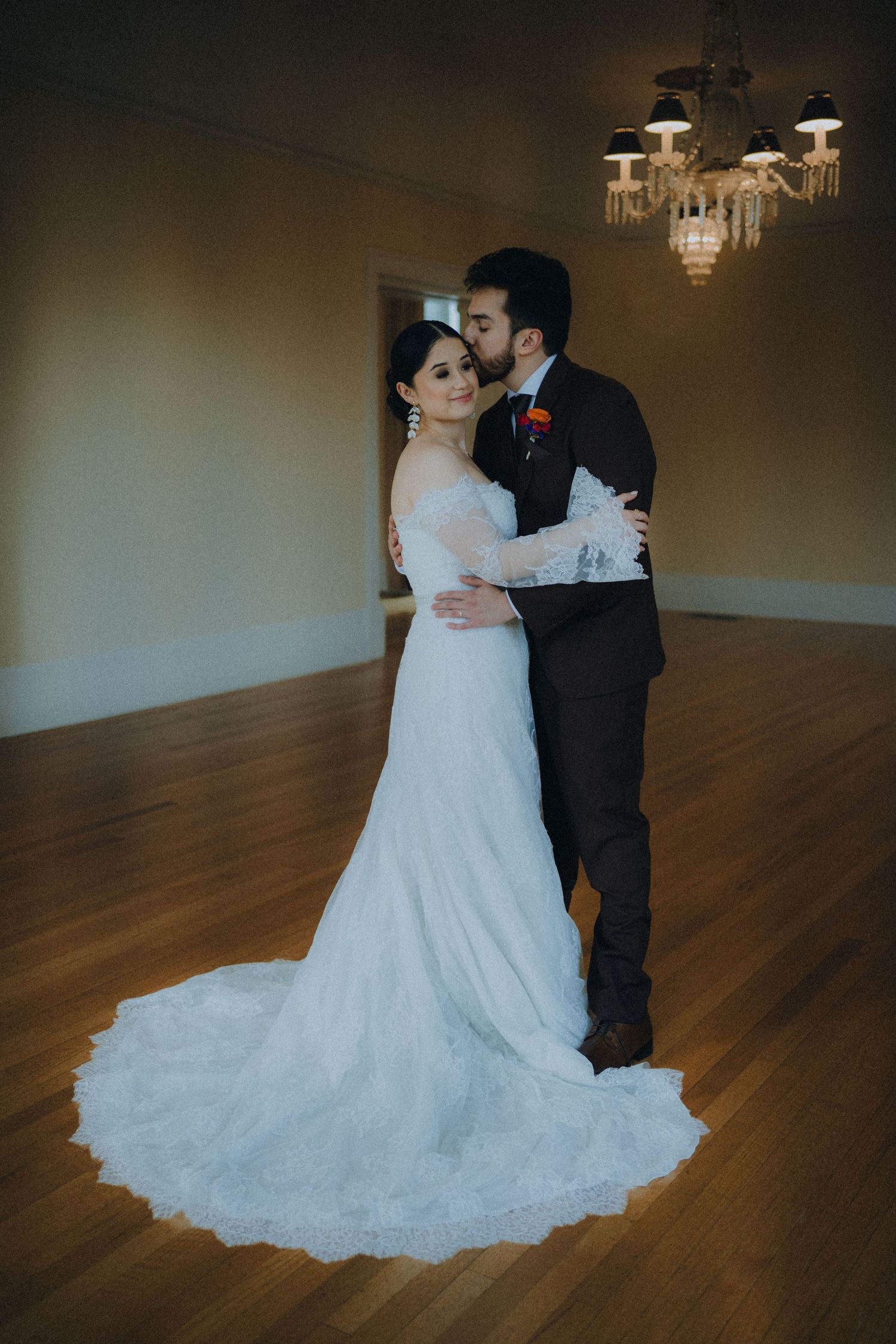 A couple in wedding attire dance together on a polished wooden floor under soft lighting in an elegant venue.