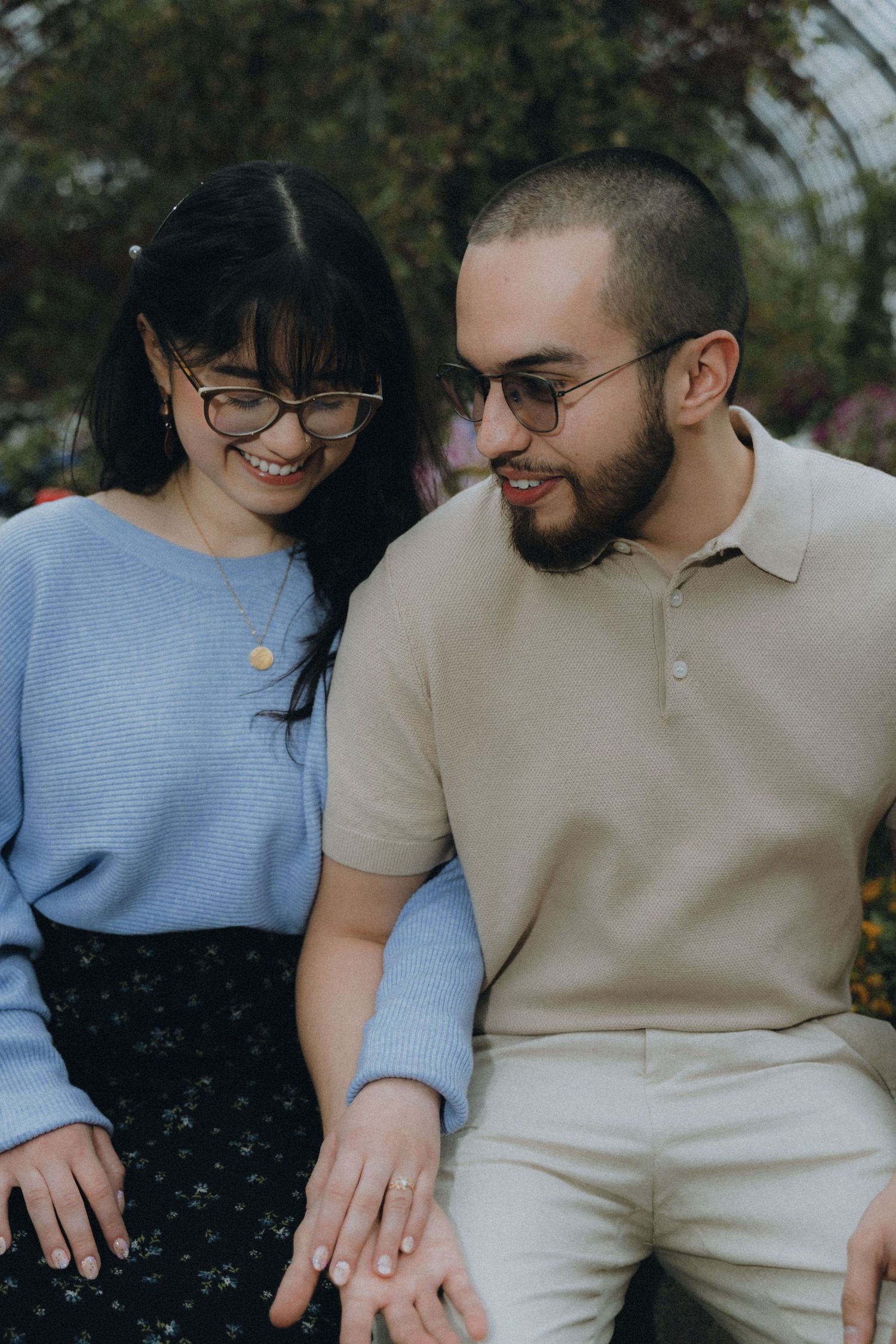 A couple sits close together outdoors wearing casual clothing in soft natural lighting.