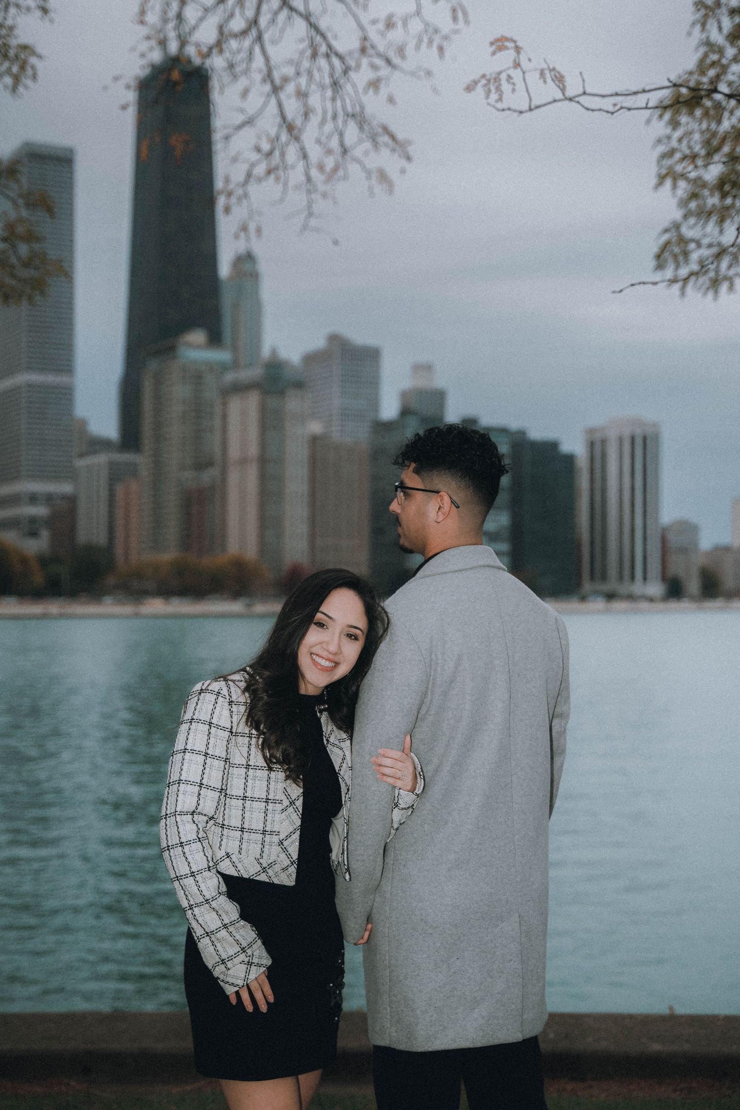 A couple shares a romantic moment along Lake Michigan with the Chicago skyline in the background on an overcast day.