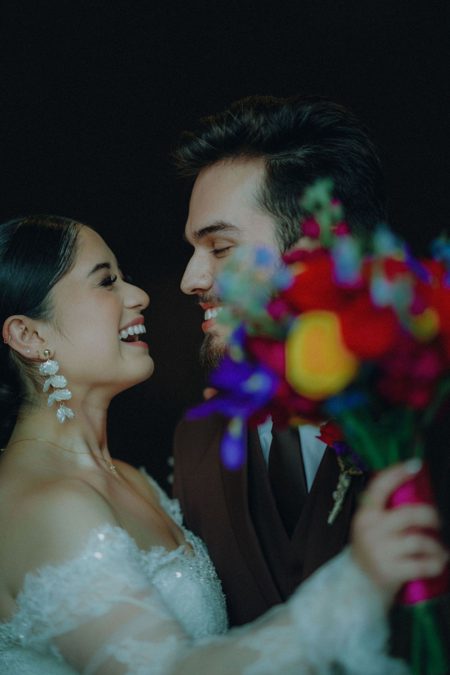 A romantic wedding couple share intimate moments in a series of dark photos with colorful floral accents.