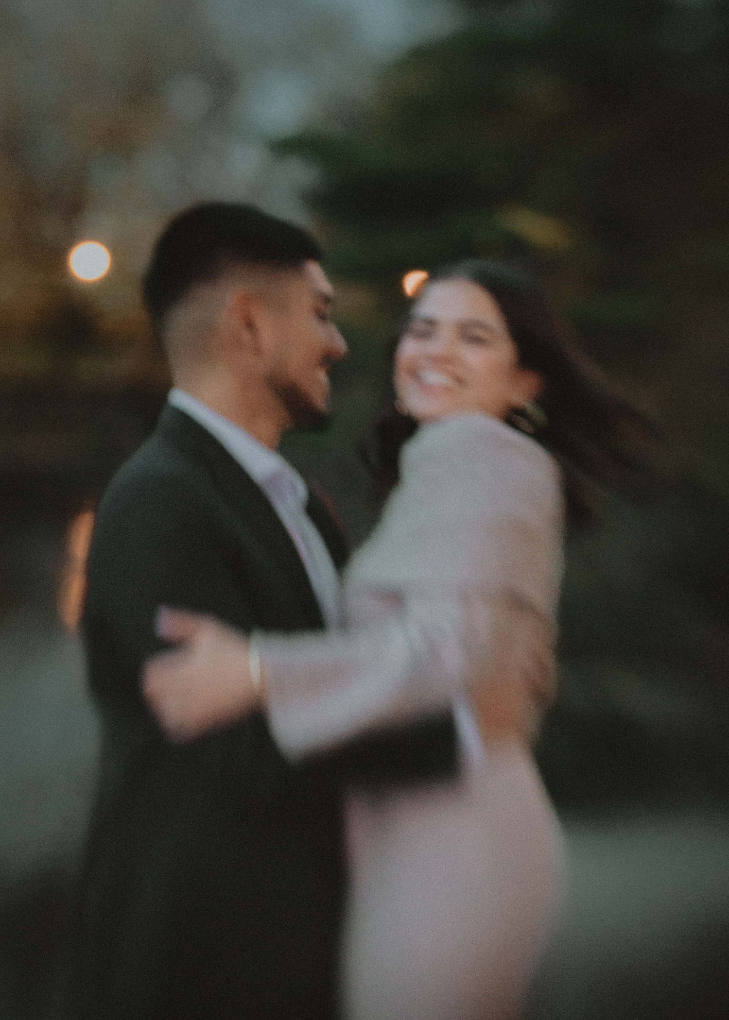 A couple shares an intimate dance together at dusk with soft bokeh lighting creating a romantic atmosphere.