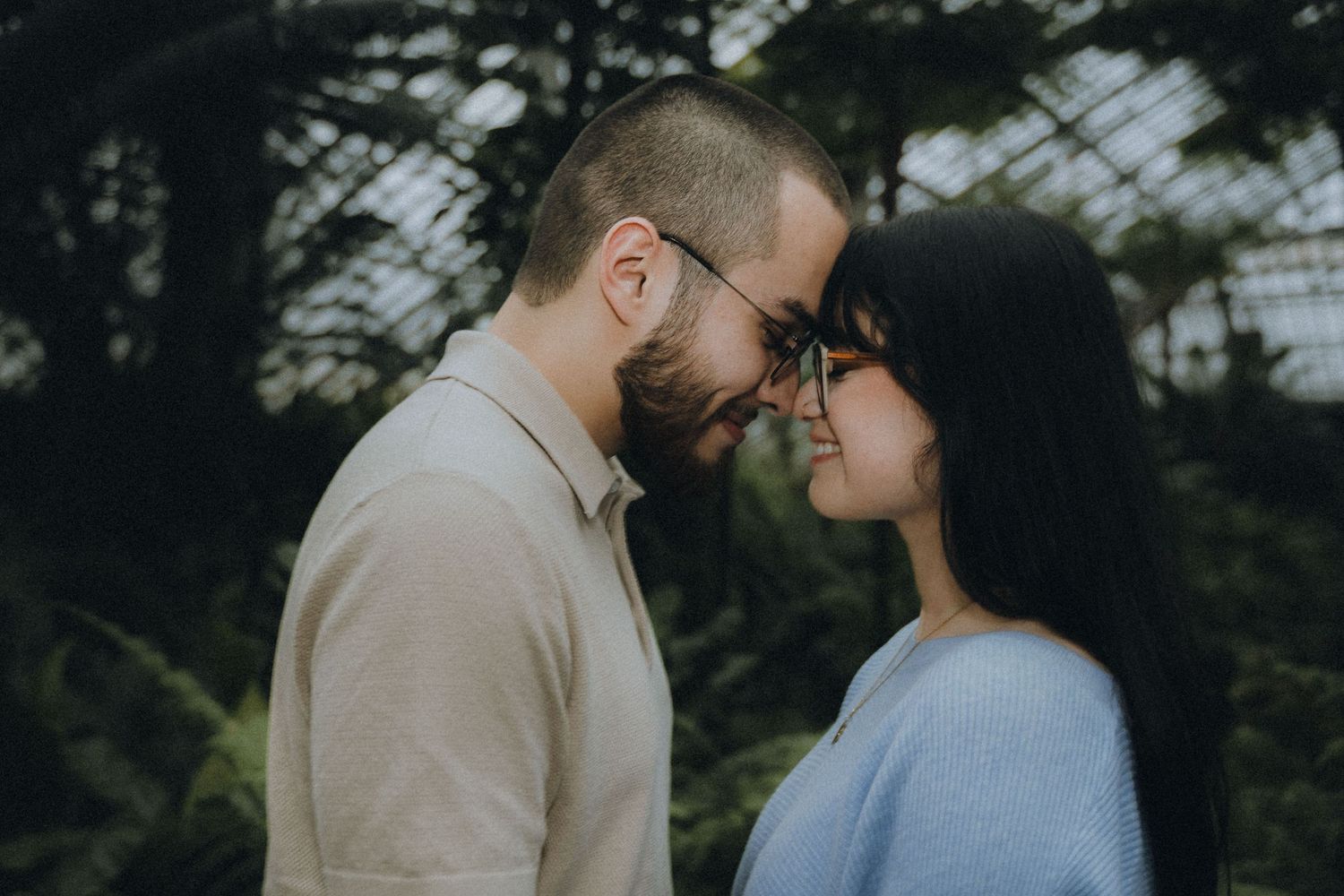A couple in casual attire share an intimate moment together in a wooded outdoor setting.