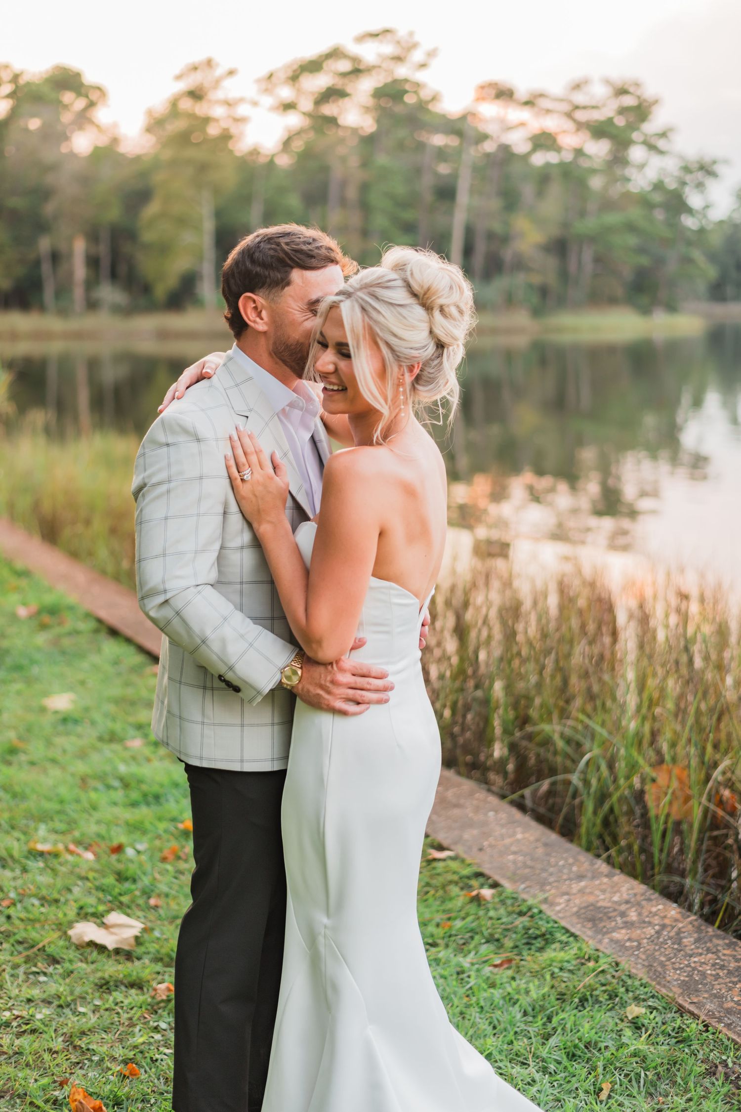 Romantic couple shares intimate moments by a serene lake with tall grasses at sunset.