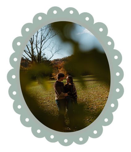 Couple embracing in a lush autumn field, framed by a decorative scalloped oval border in soft sage green.