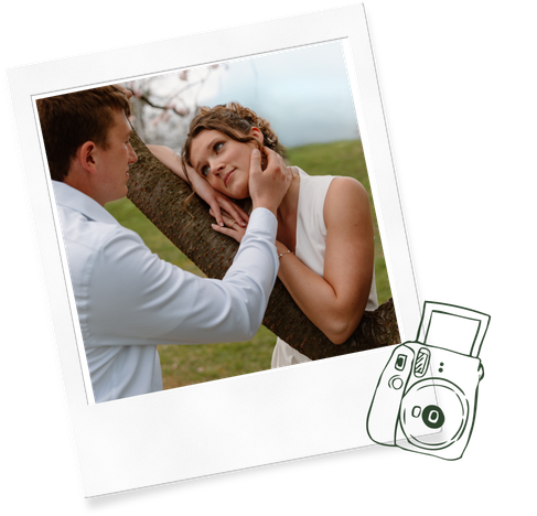 A romantic couple shares a tender moment by a tree, the groom gently cupping the bride's face outdoors.