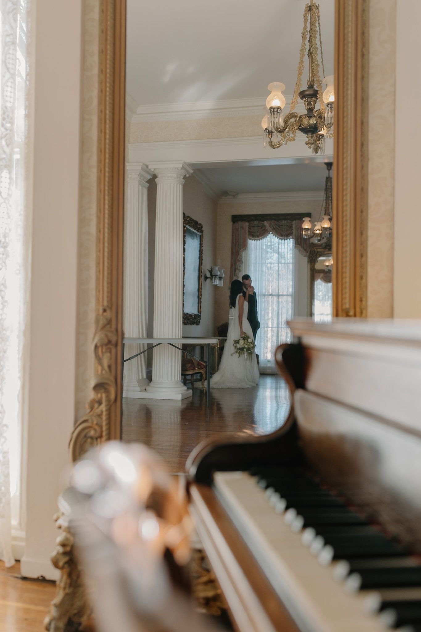 Elegant interior hallway with ornate gold mirrors, white columns and chandelier lighting.