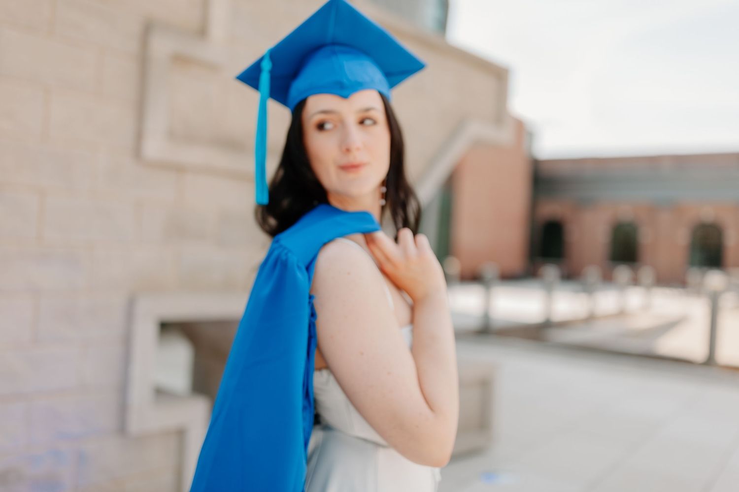 A graduation photoshoot featuring bright blue academic regalia against a light stone building backdrop.