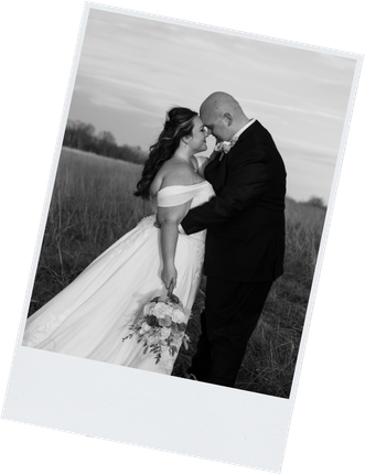 Black and white polaroid photo of a bride and groom sharing an intimate moment in a field at dusk.