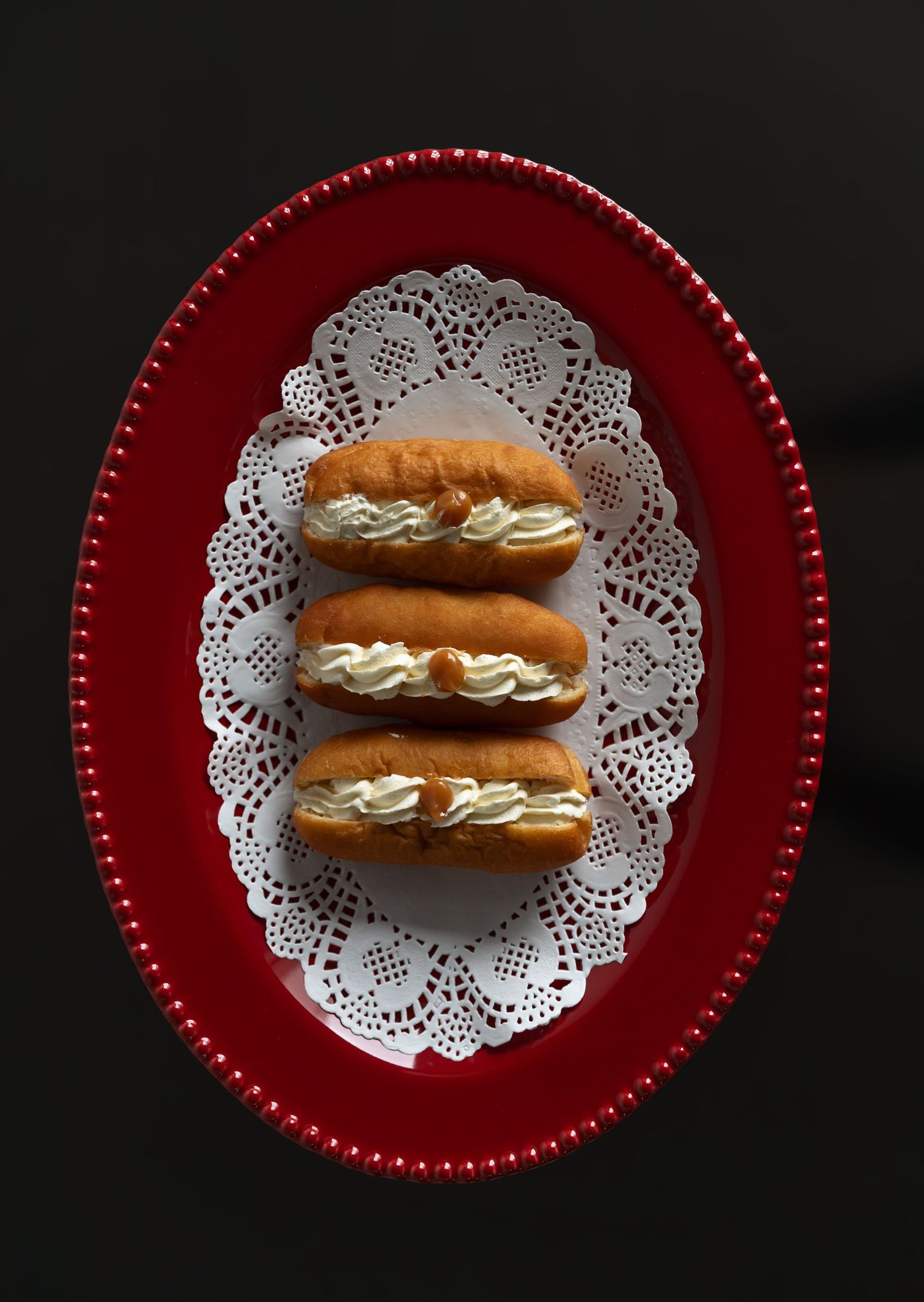 Three cream-filled whoopie pies arranged on a white doily placed on an elegant red oval platter against dark background.