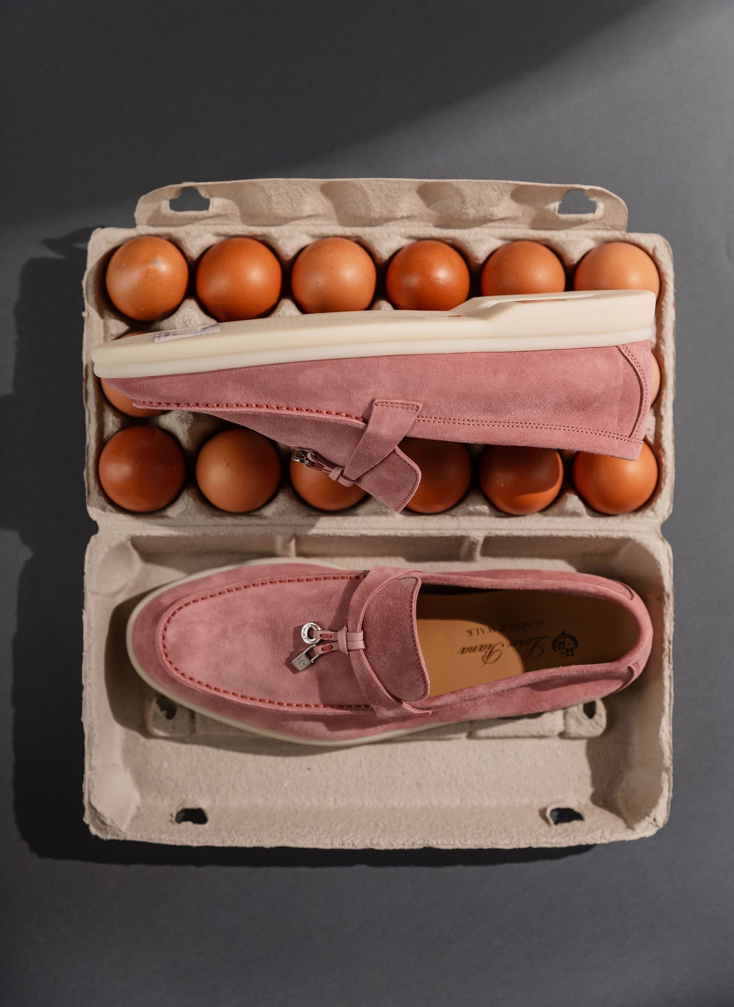 Creative arrangement shows pink suede loafers placed neatly in an egg carton, creating a unique visual comparison.