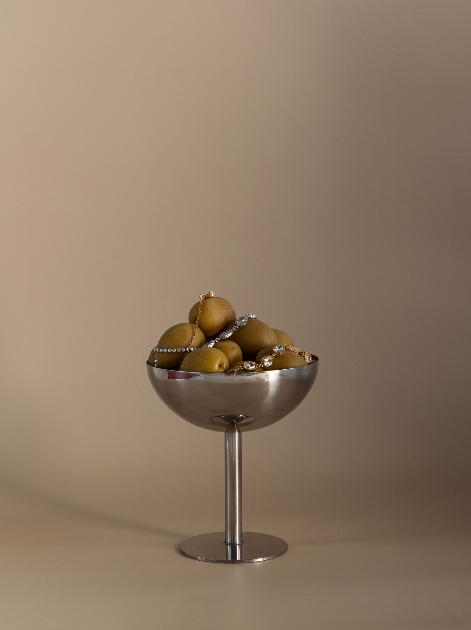 A series of four identical silver pedestal bowls filled with olives shown at different angles against a neutral background.