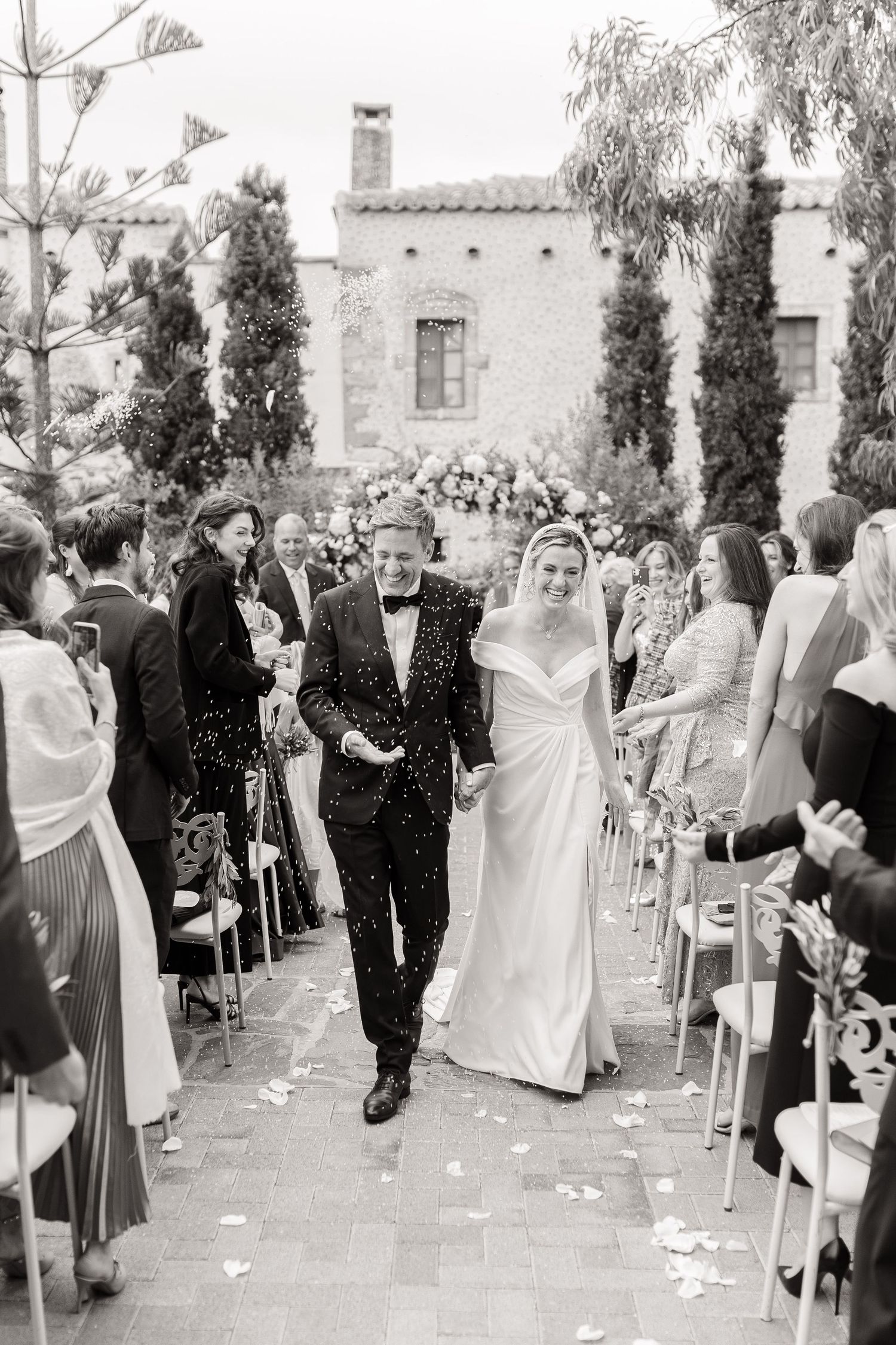 Bride and groom walk down the aisle as guests toss confetti at an elegant outdoor wedding ceremony.
