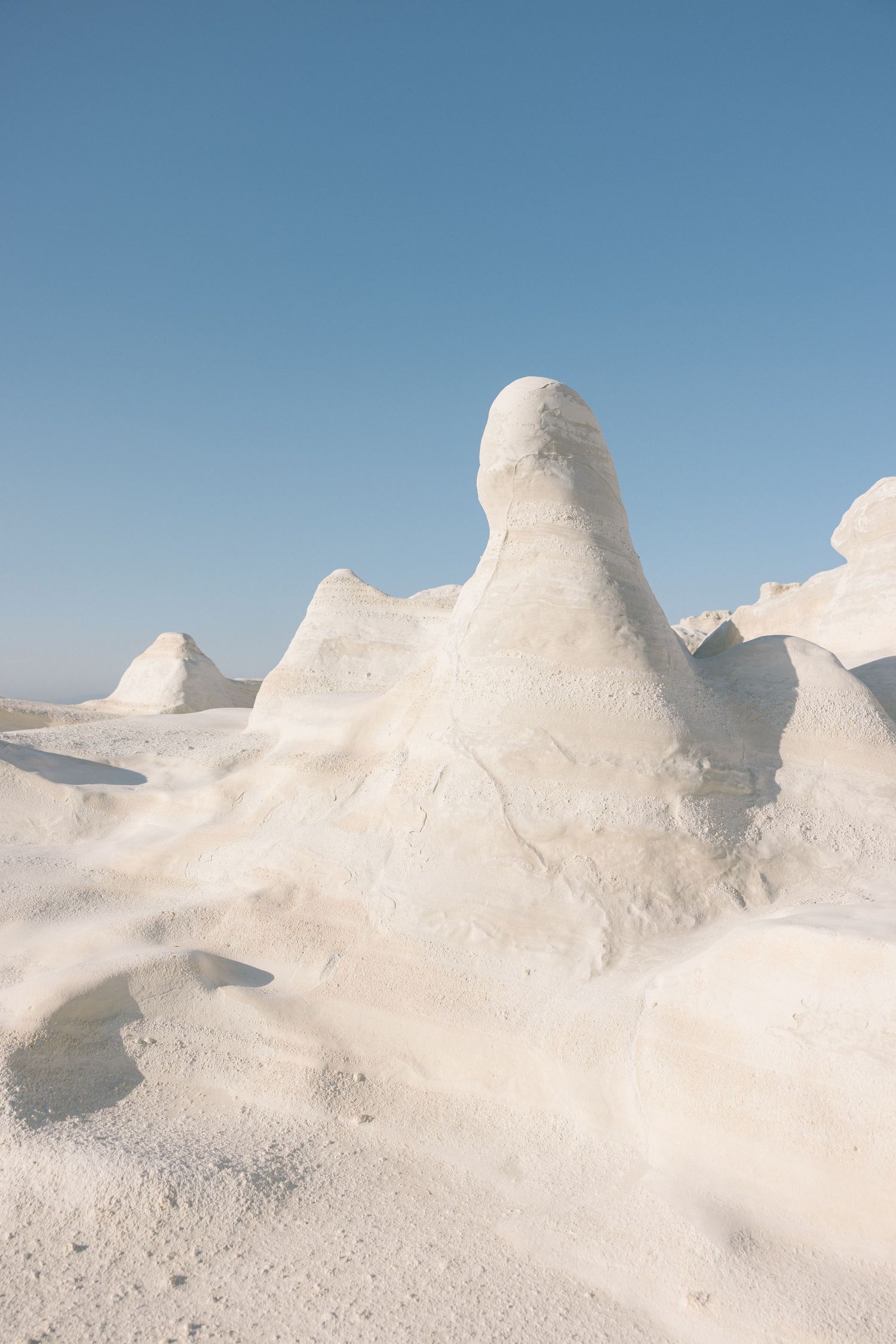 Smooth white rock formations with rounded peaks and valleys create an otherworldly landscape against a bright blue sky.